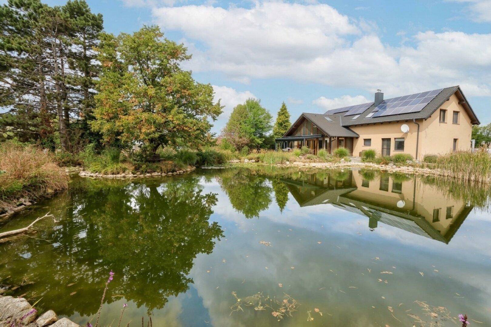 Charmantes Haus mit großem Teich und grüner Umgebung unter einem weiten Himmel.