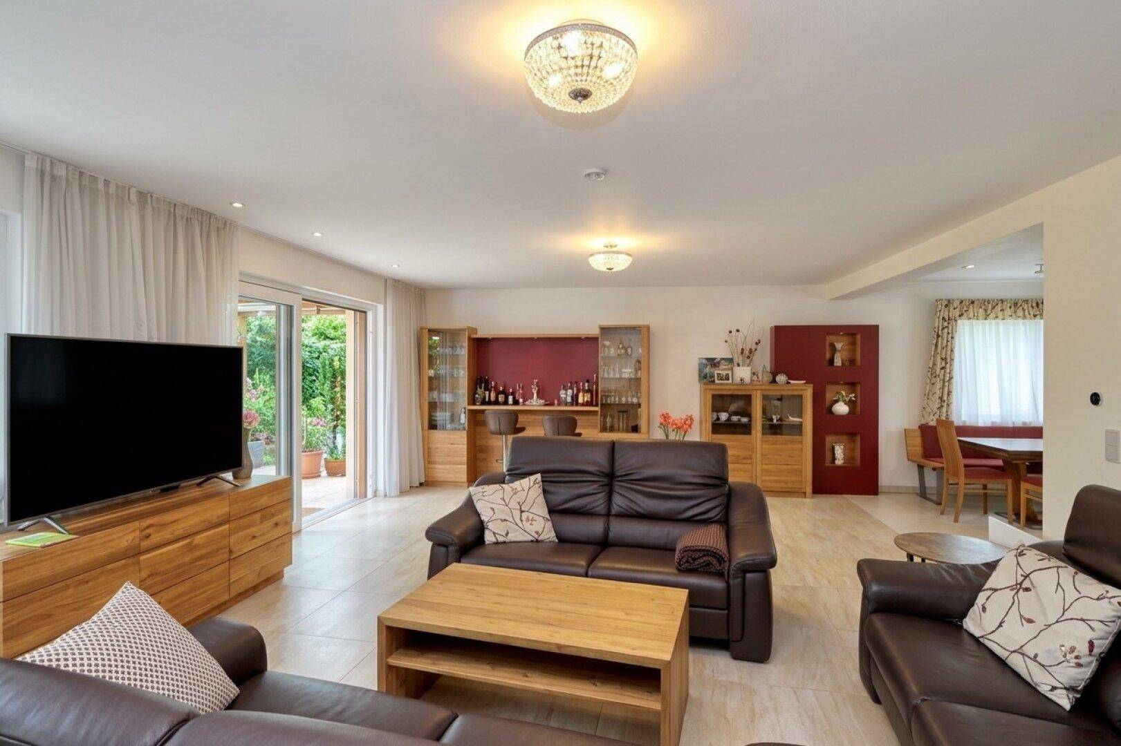 Geräumiges Wohnzimmer mit bequemen Ledersofas, Fliesenboden und Blick in den Garten.