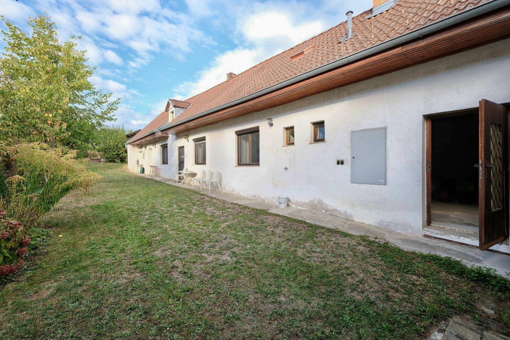 Lange Gebäudefassade mit mehreren Fenstern und einer Tür, die zu einem grünen Gartenbereich führt.