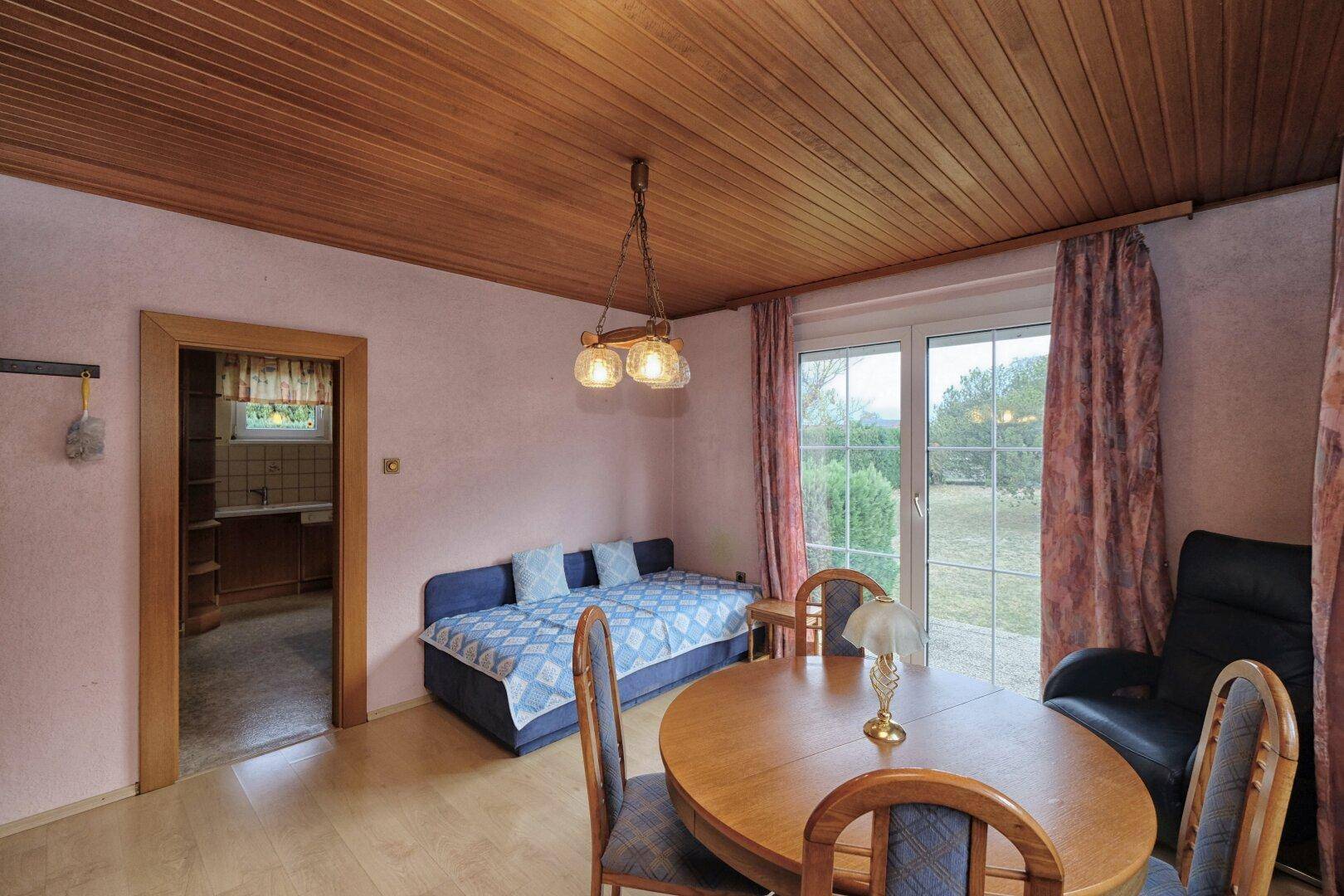 Essbereich mit Holztäfelung, Tagesbett und direktem Zugang zum Garten durch eine Terrassentür.