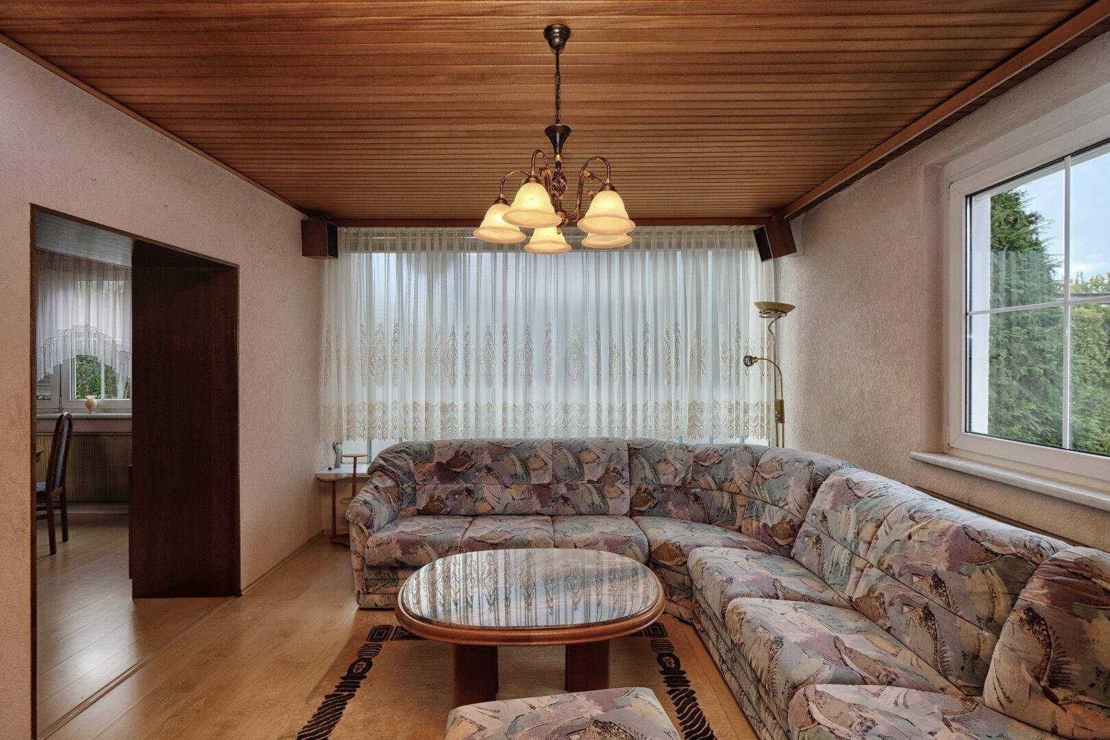 Geräumiges Wohnzimmer mit großer Eckcouch, Holztäfelung an der Decke und Laminatboden.