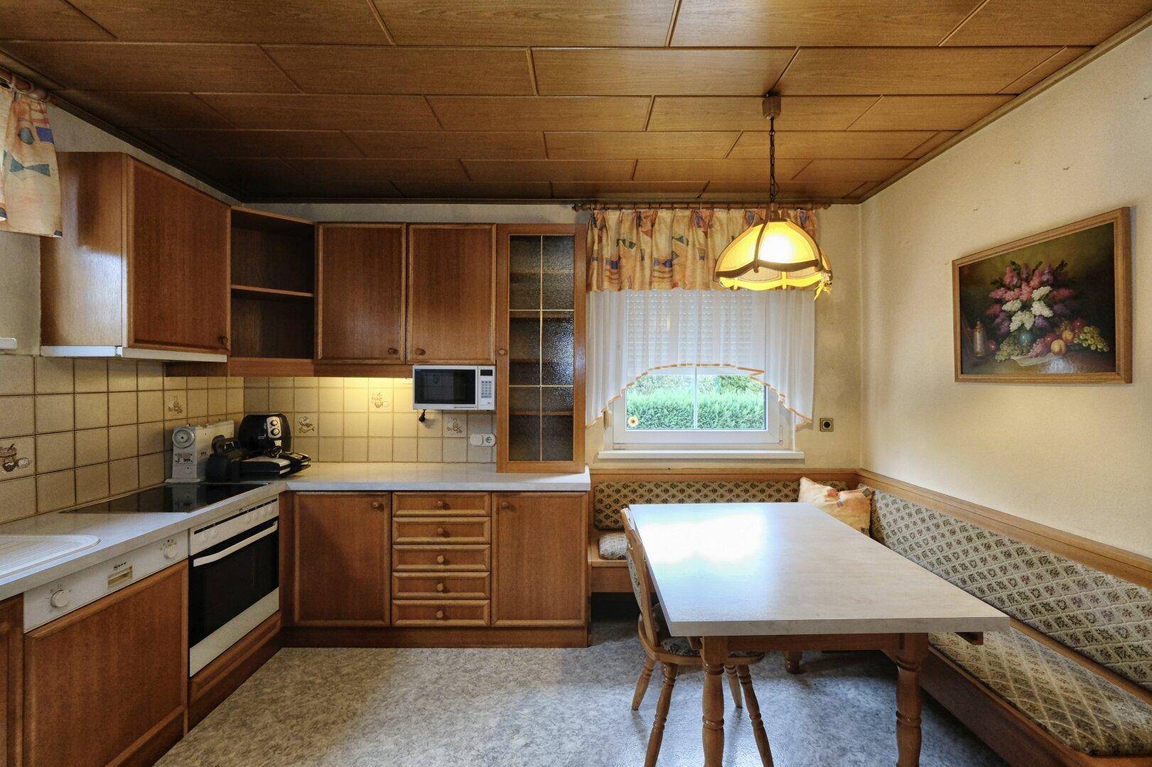 Traditionelle Wohnküche mit Holzeinbauten, Fliesenrückwand und integriertem Essbereich.