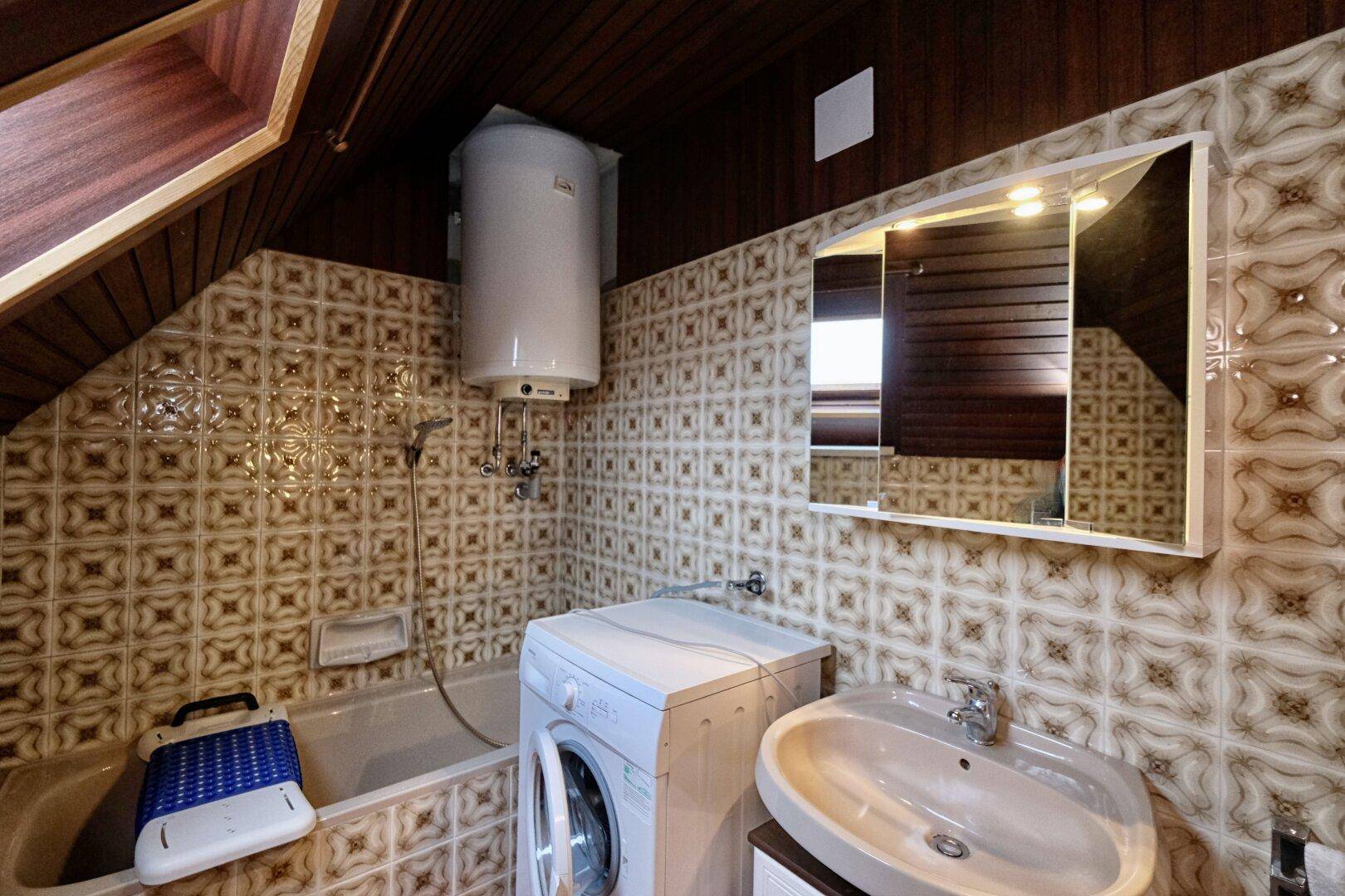 Badezimmer im Dachgeschoss mit Badewanne, Waschmaschine und gemusterten Fliesen.