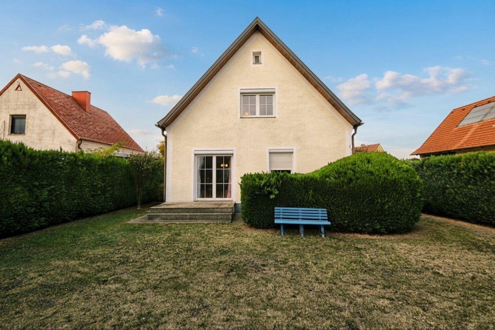 Rückseite des Hauses mit gepflegtem Rasen, Hecke und einer kleinen blauen Bank.