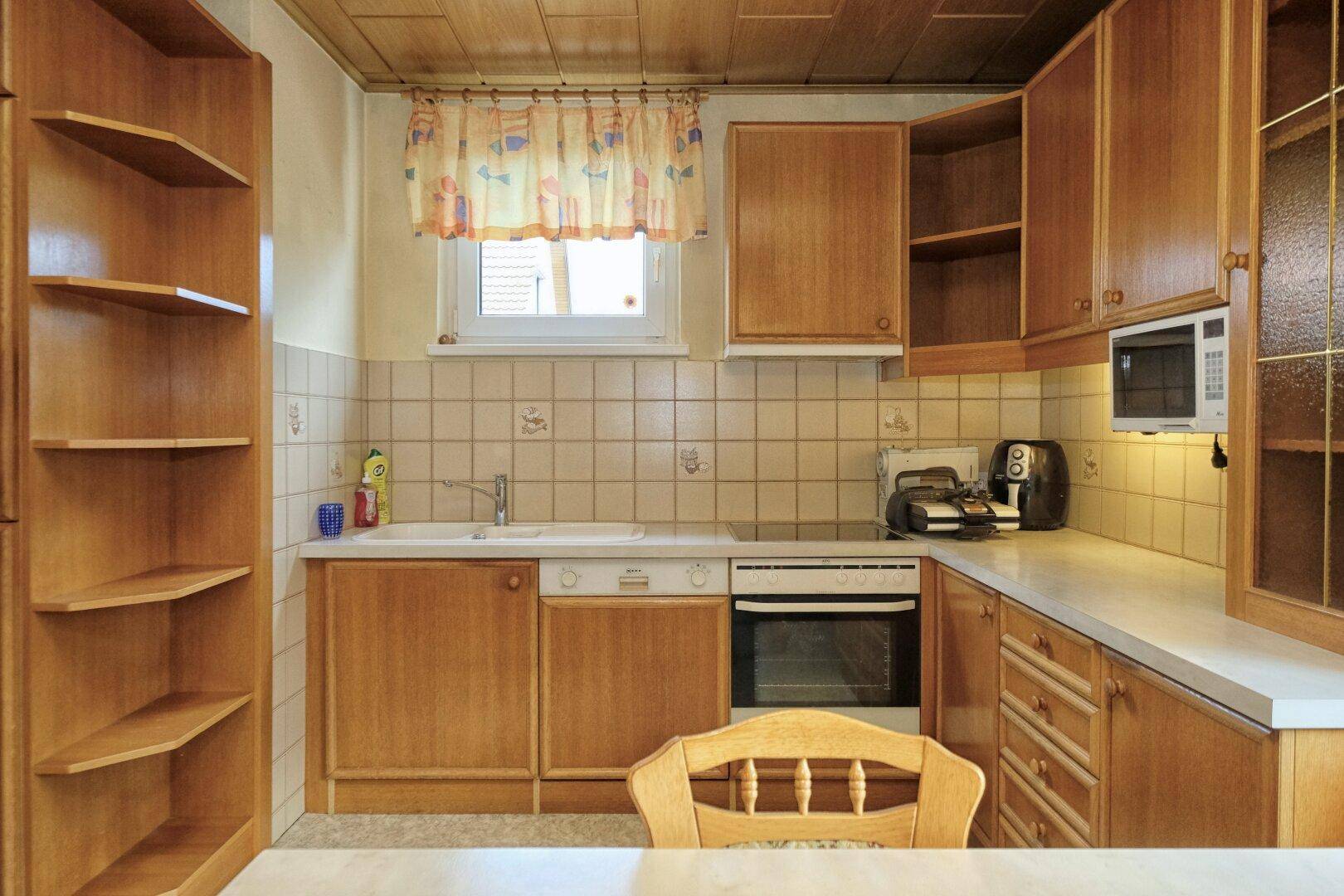Funktionale Küche mit Holzschränken, weißen Arbeitsplatten und einem Fenster über der Spüle.
