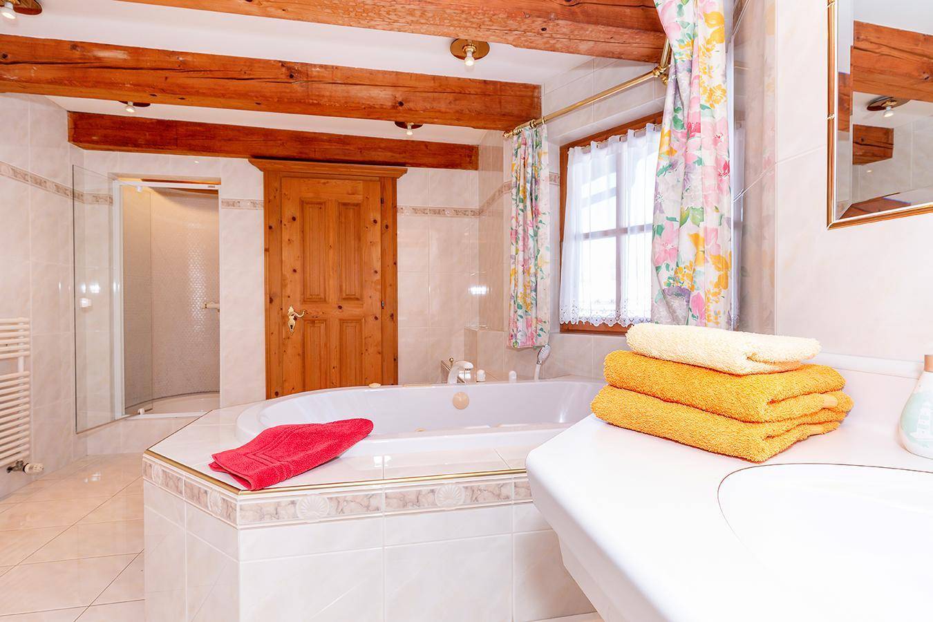 Detailansicht eines Badezimmers mit Eckbadewanne, Waschbecken und Holzbalken.