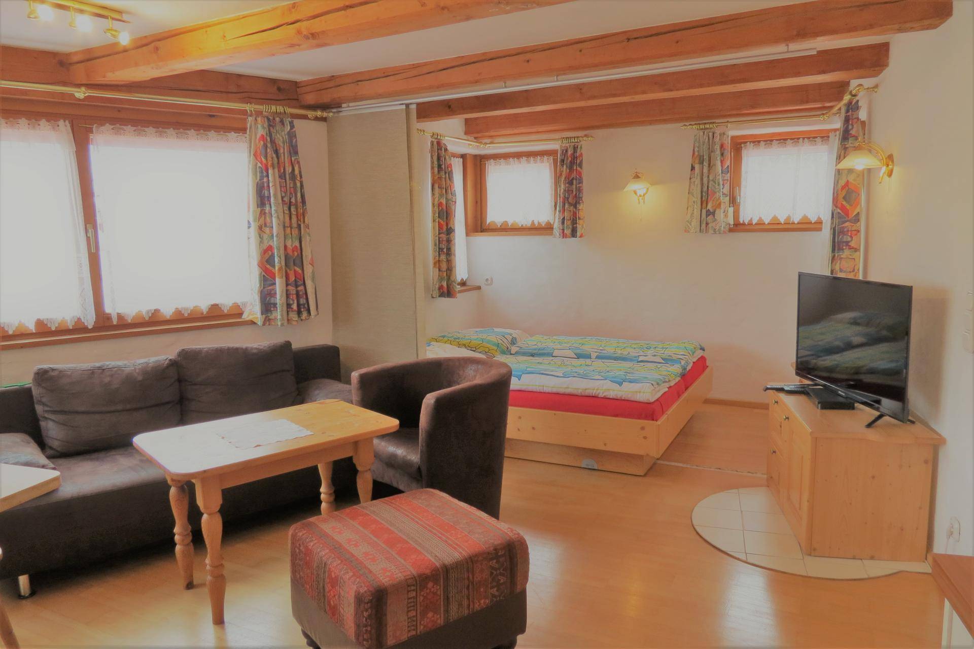 Gemütlicher Wohnbereich mit Sofa, Fernseher und Holzbalken unter dem Dach.