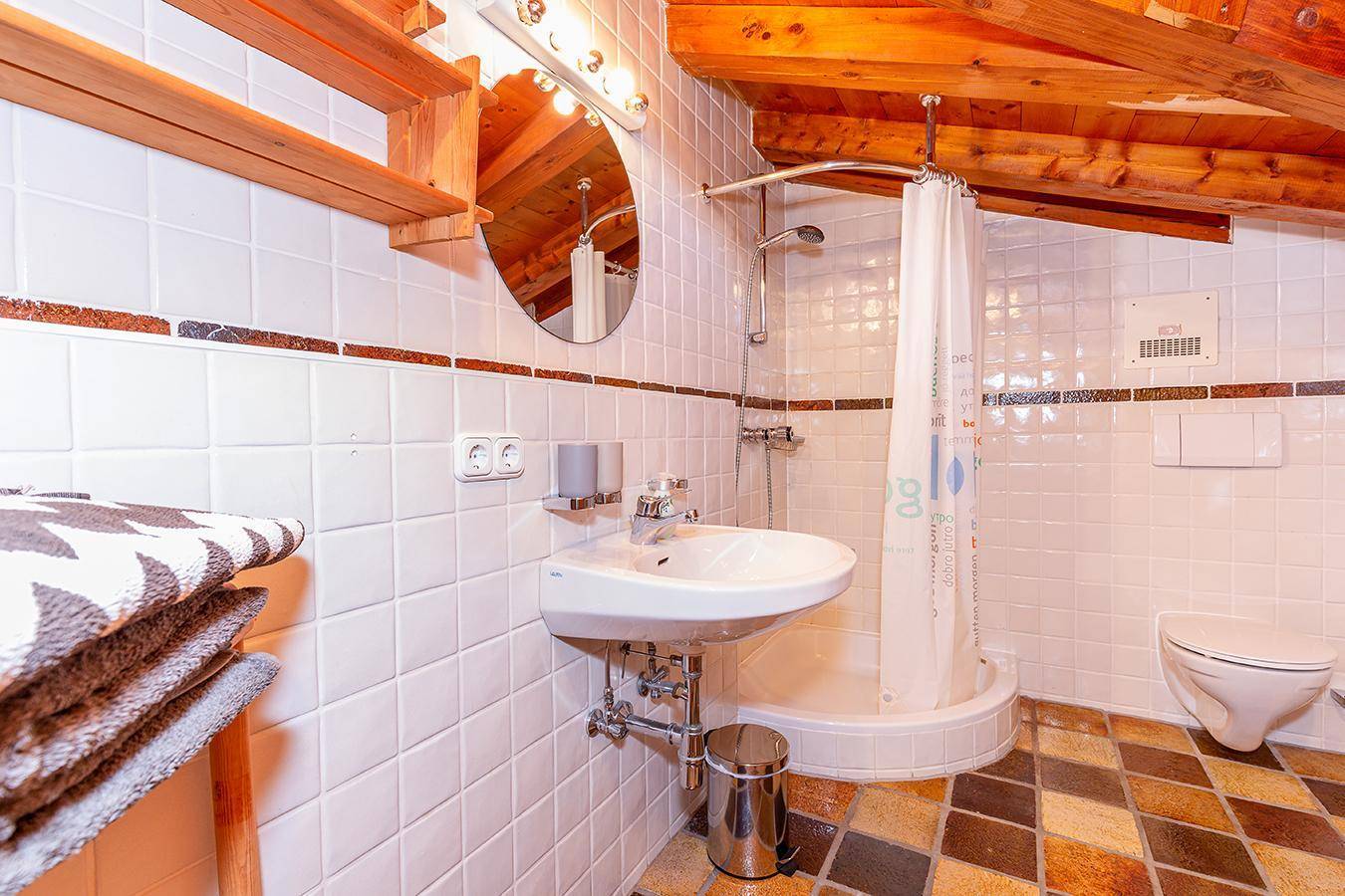 Badezimmer mit Dusche, Waschbecken und Holzbalken unter dem Dach.