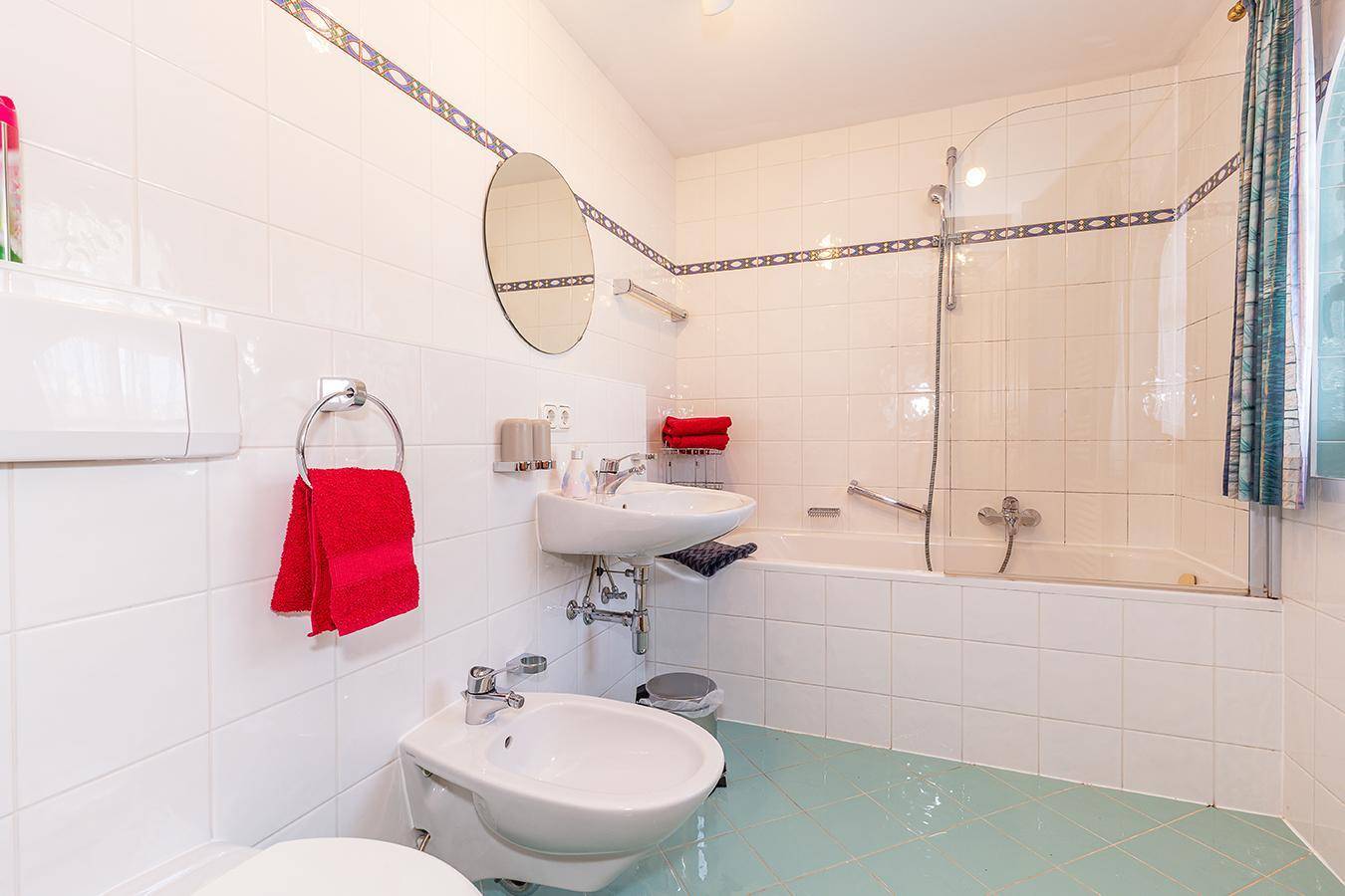 Helles Badezimmer mit weißen Fliesen, Badewanne mit Duschabtrennung und Bidet.