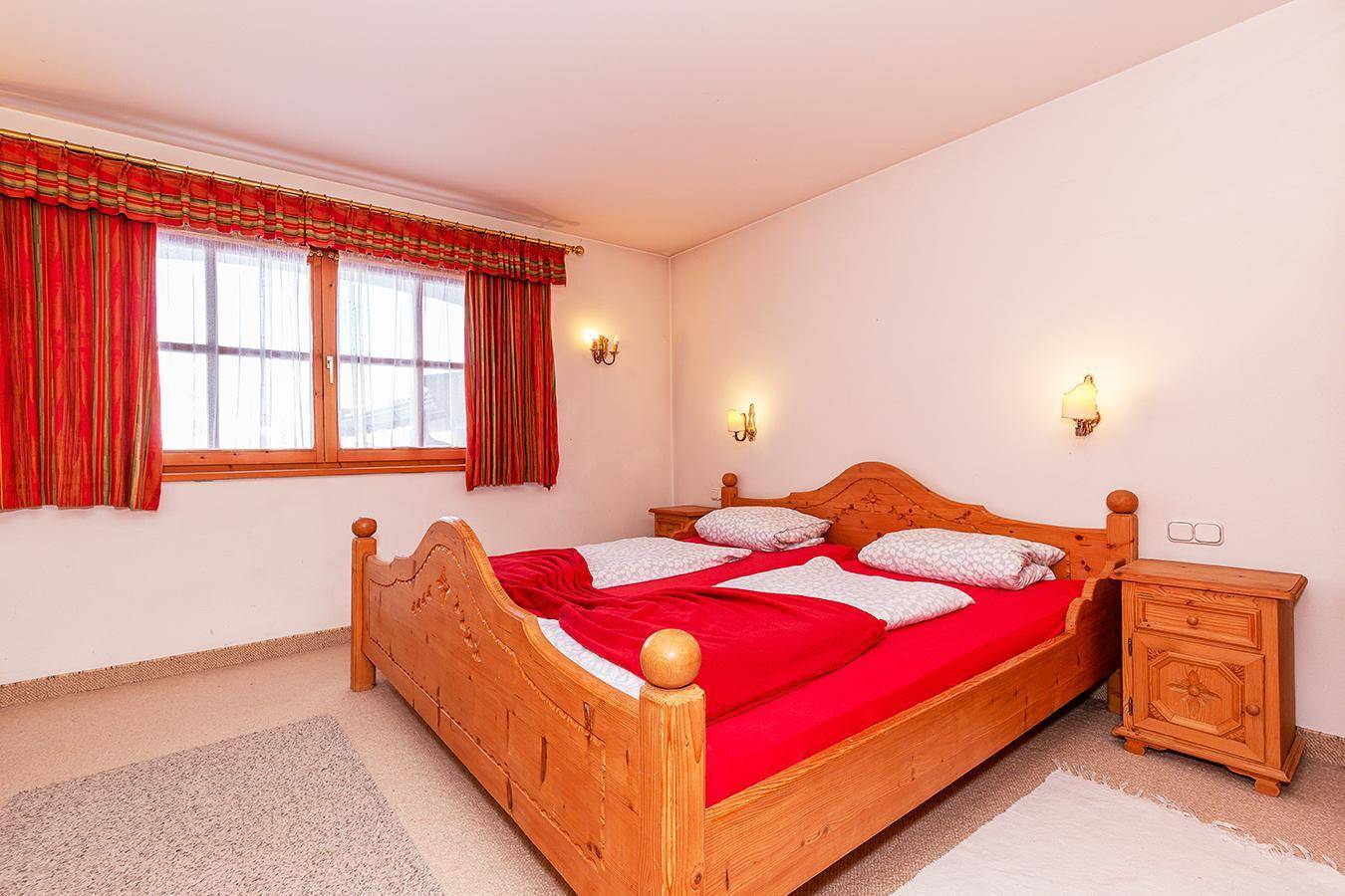 Gemütliches Schlafzimmer mit traditionellem Holzdoppelbett, roten Vorhängen und Teppichboden.