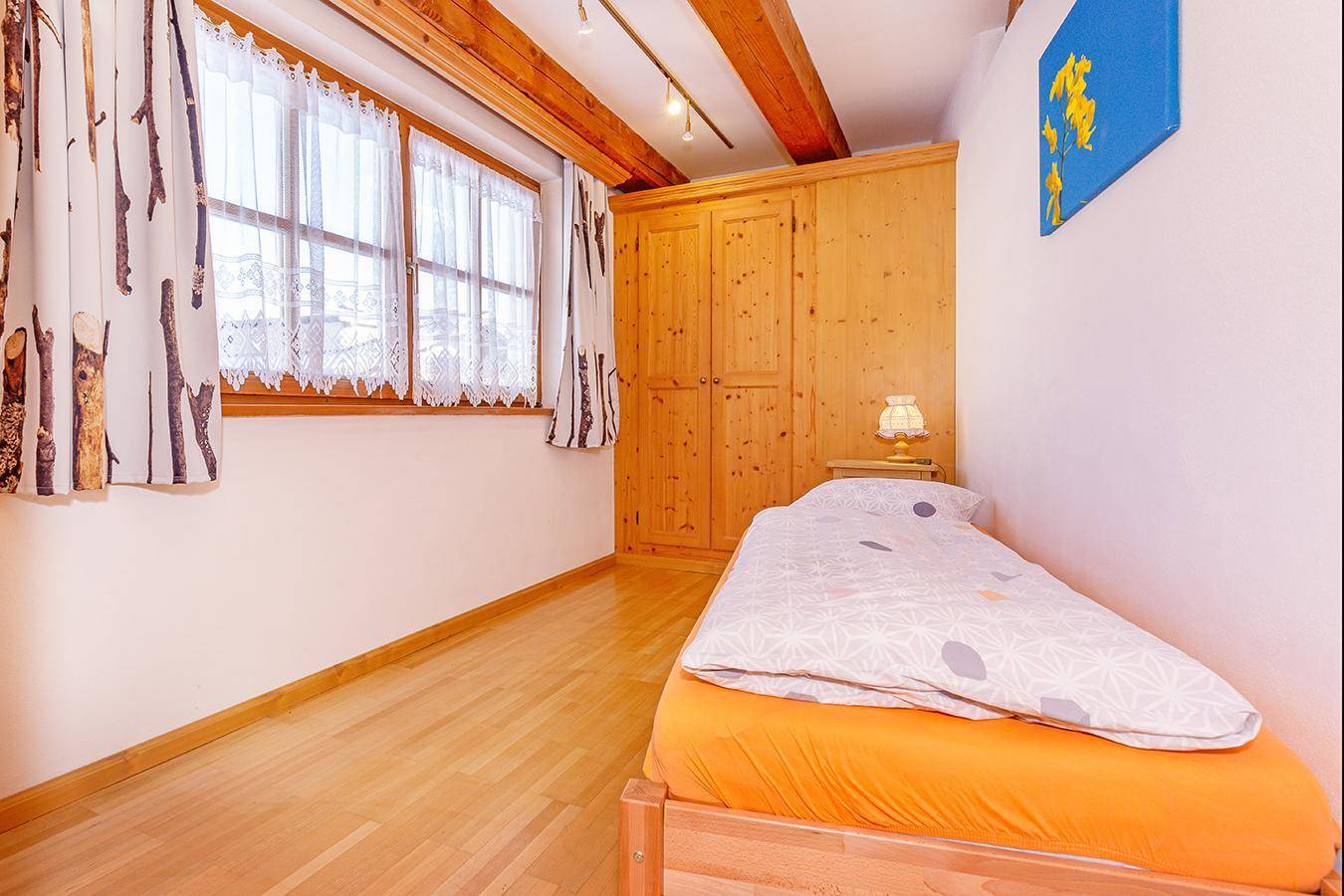 Helles Schlafzimmer mit Einzelbett, Einbauschrank und Holzbalken an der Decke.