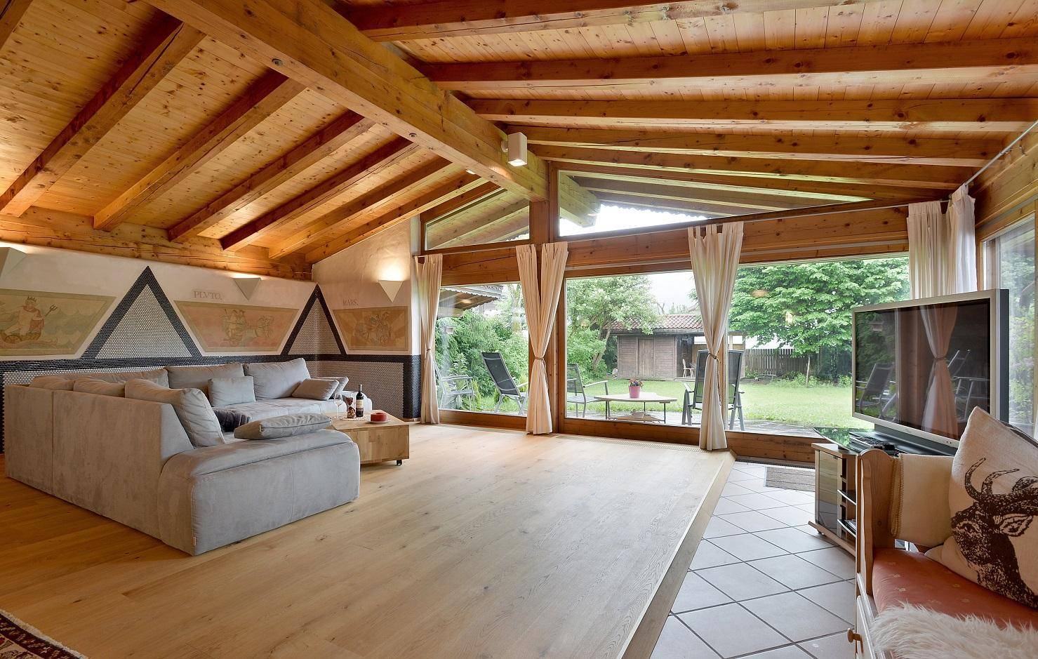 Geräumiges Wohnzimmer mit Holzbalkendecke, großen Fenstern und Blick in den Garten.