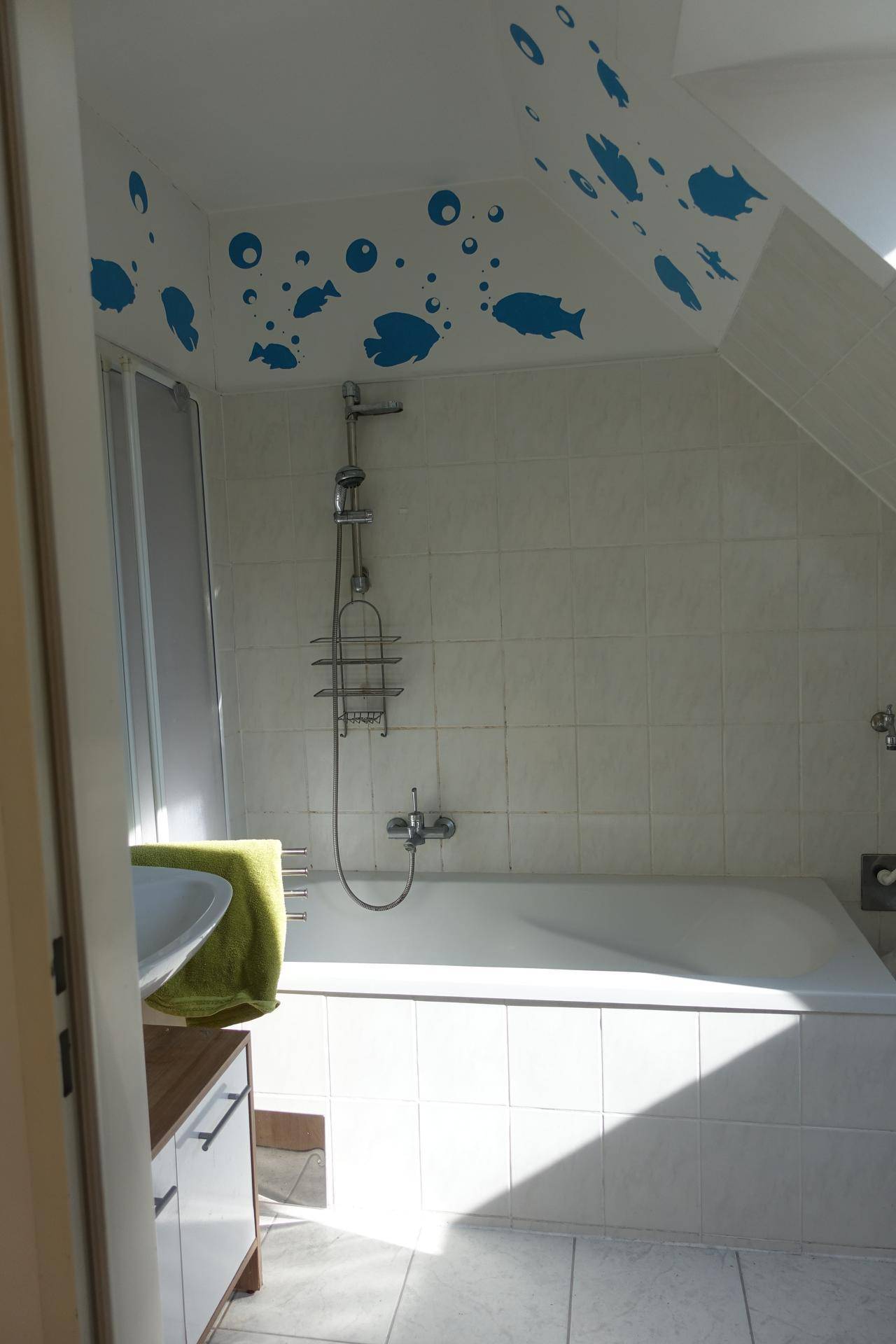 Helles Badezimmer mit Badewanne, weißen Fliesen und verspielten Fischmotiven an der Wand.
