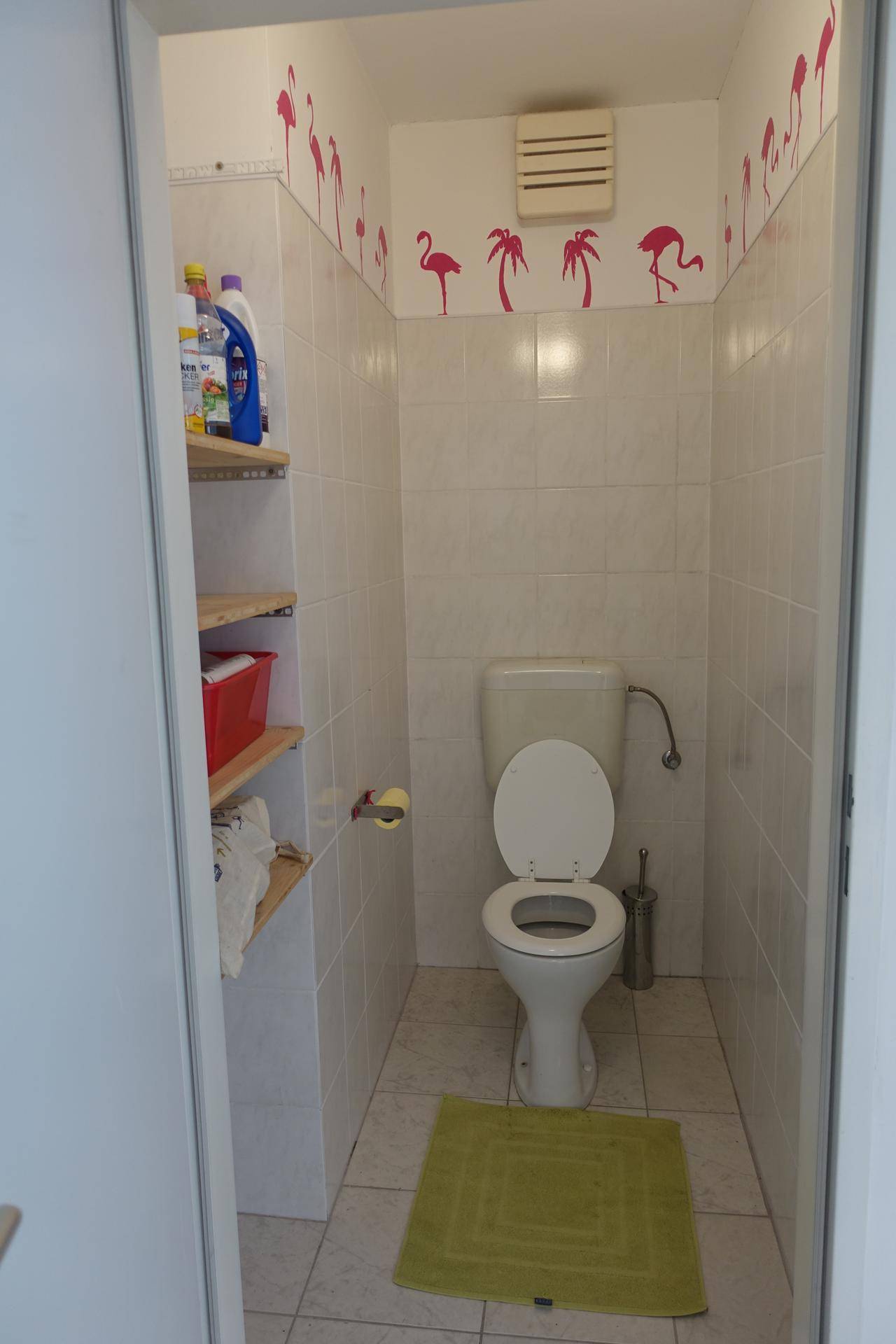 Kleines WC mit weißen Fliesen, Regal und pinken Flamingo-Wandstickern.