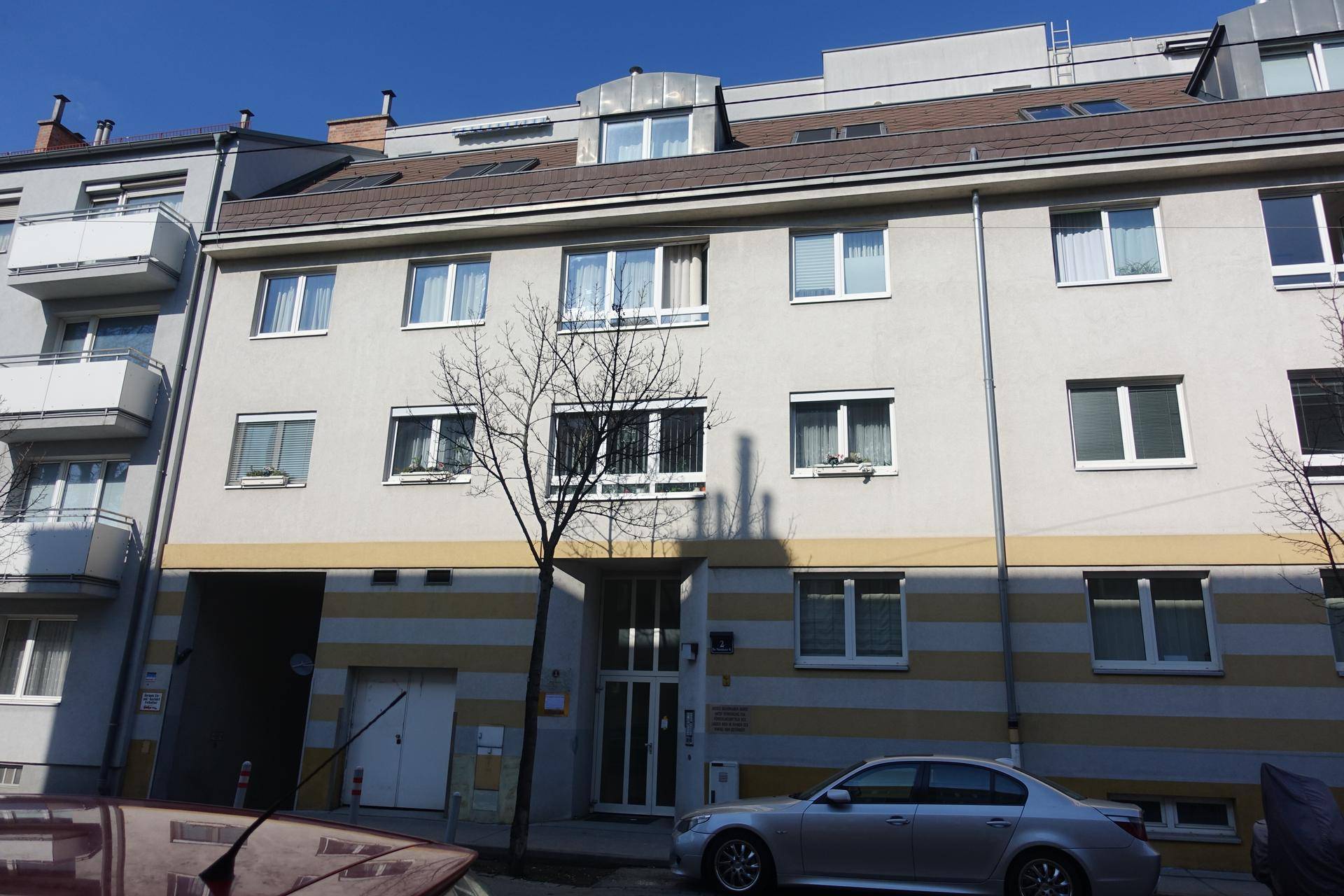 Mehrfamilienhaus mit moderner Fassade, Balkonen und Dachgeschosswohnungen unter blauem Himmel.
