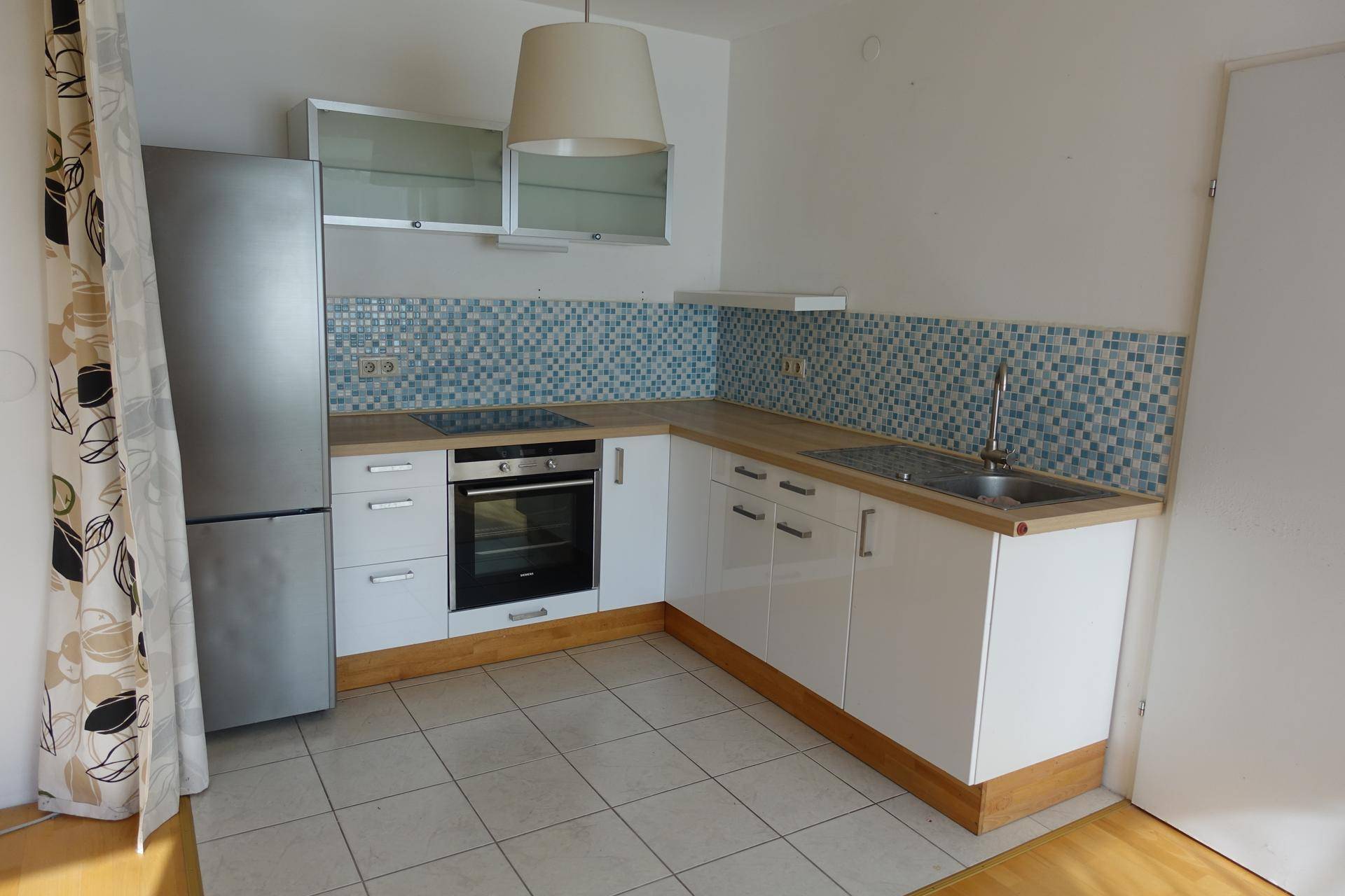 Funktionale Küche mit weißen Schränken, Holzarbeitsplatte und blauen Mosaikfliesen.