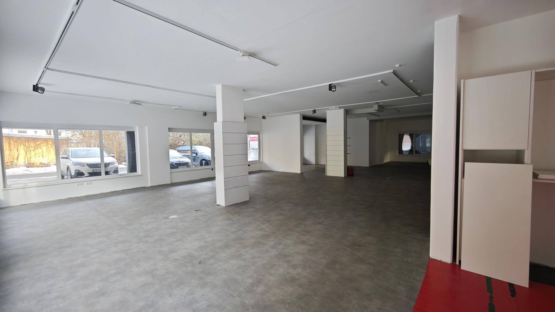 Geräumiger, leerer Geschäftsraum mit großen Fenstern, Betonboden und weißen Wänden, bereit zur Gestaltung.