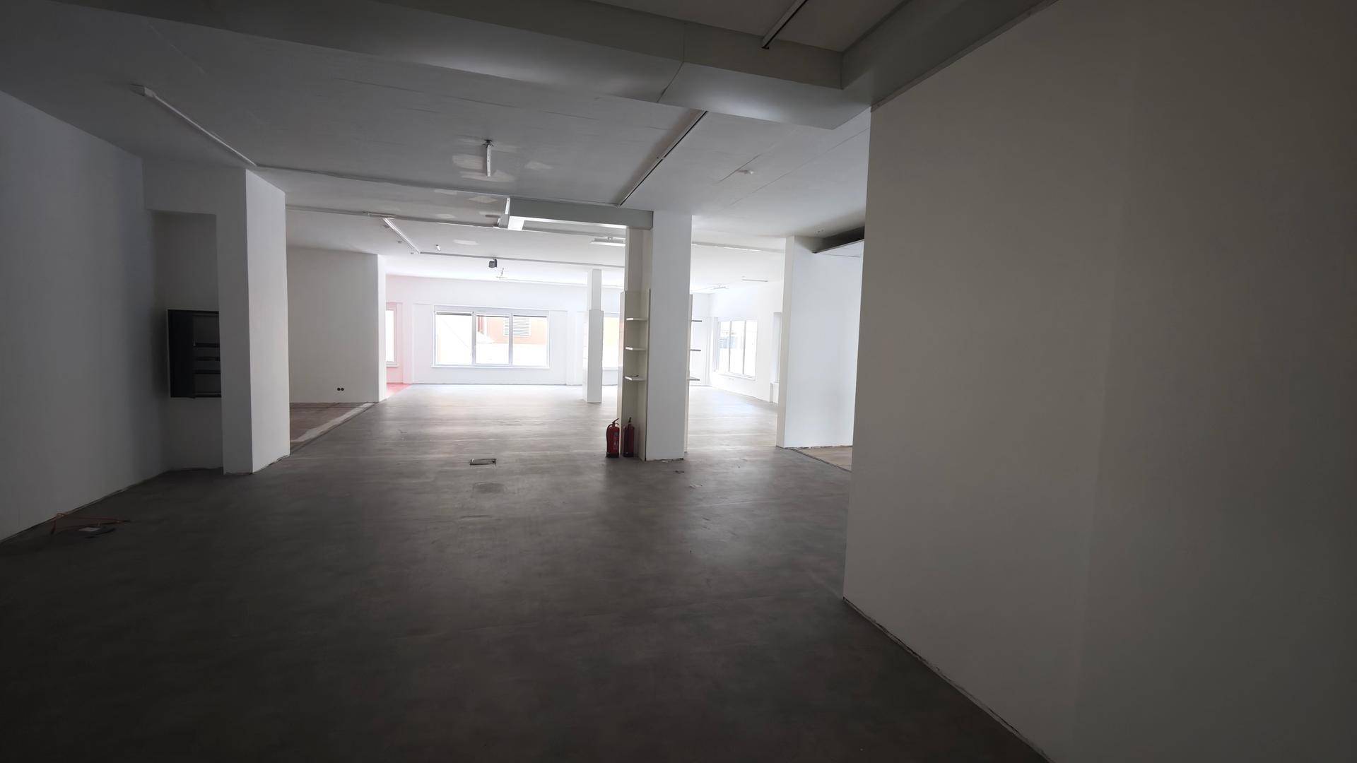 Tiefer Blick in den weitläufigen, leeren Geschäftsraum mit durchgehenden Betonböden und hellen Wänden.