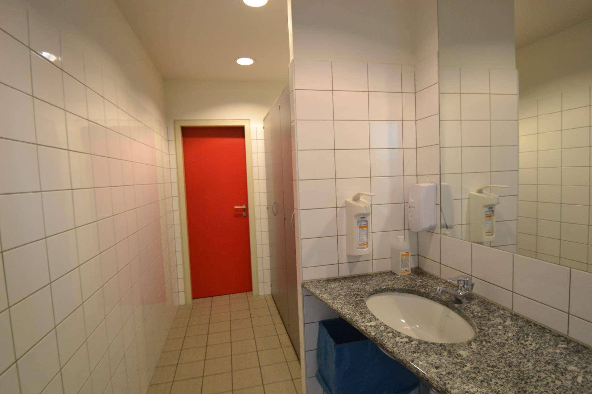 Gefliestes Badezimmer mit Waschbecken, großem Spiegel und roter Tür.