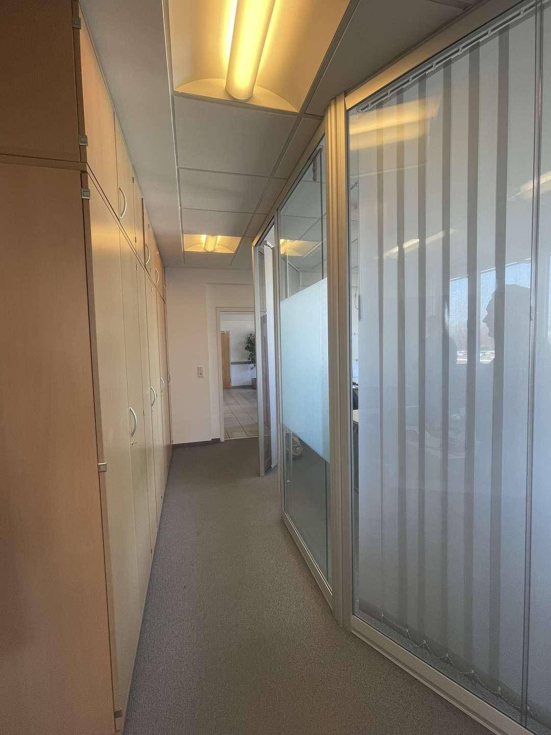 Flur mit Teppichboden, Einbauschränken und Glaswänden zu den Büroräumen.
