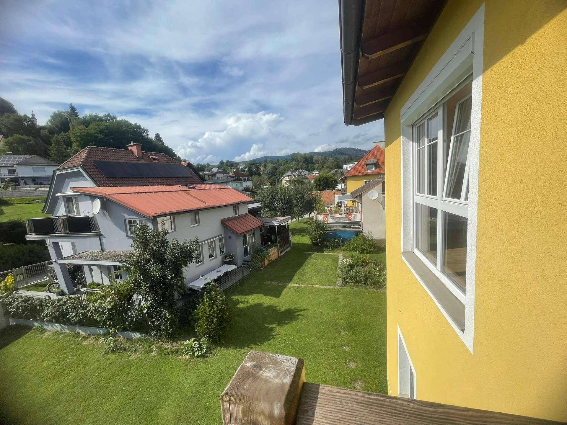 Weitläufiger Blick über die grüne Umgebung mit weiteren Häusern und Bergen im Hintergrund.