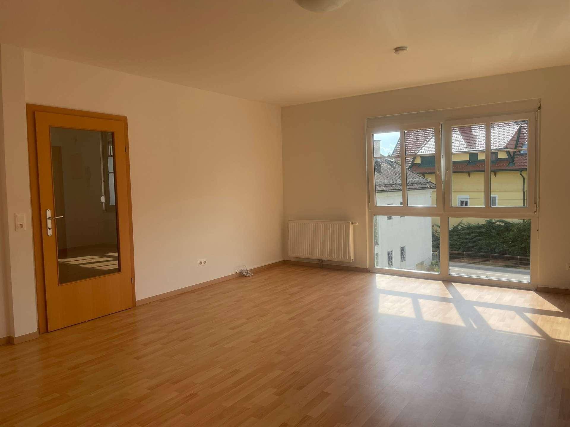 Geräumiges, helles Zimmer mit Holzboden und großen Fenstern, die viel Tageslicht hereinlassen.
