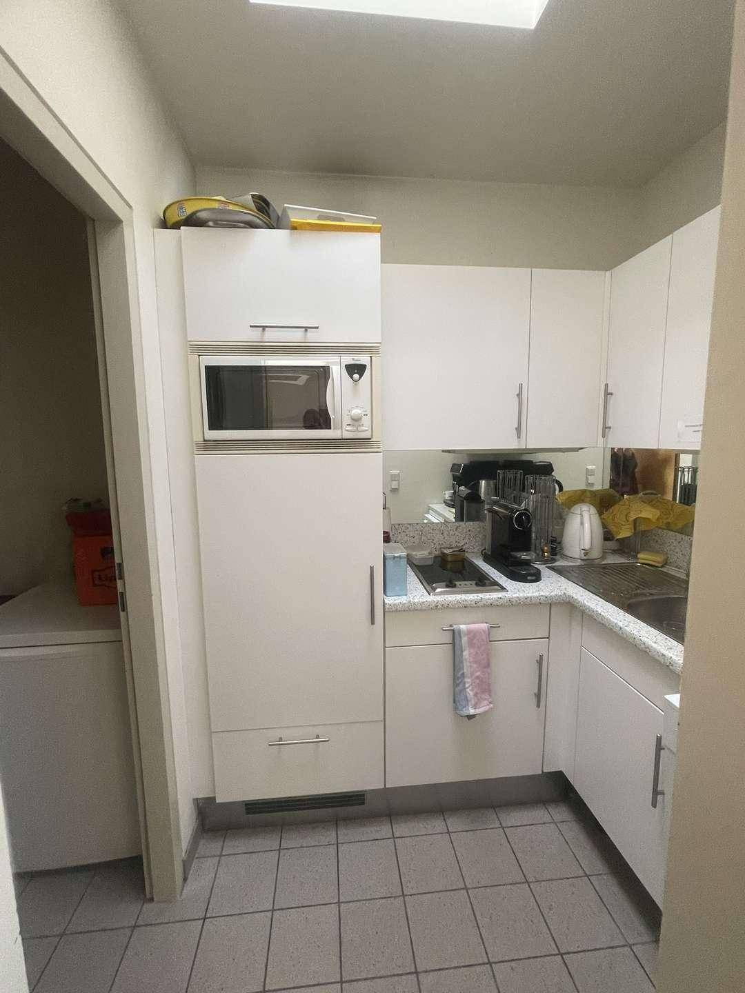 Kleine Einbauküche mit weißen Schränken, Mikrowelle und Spülbecken, ideal für Pausen.