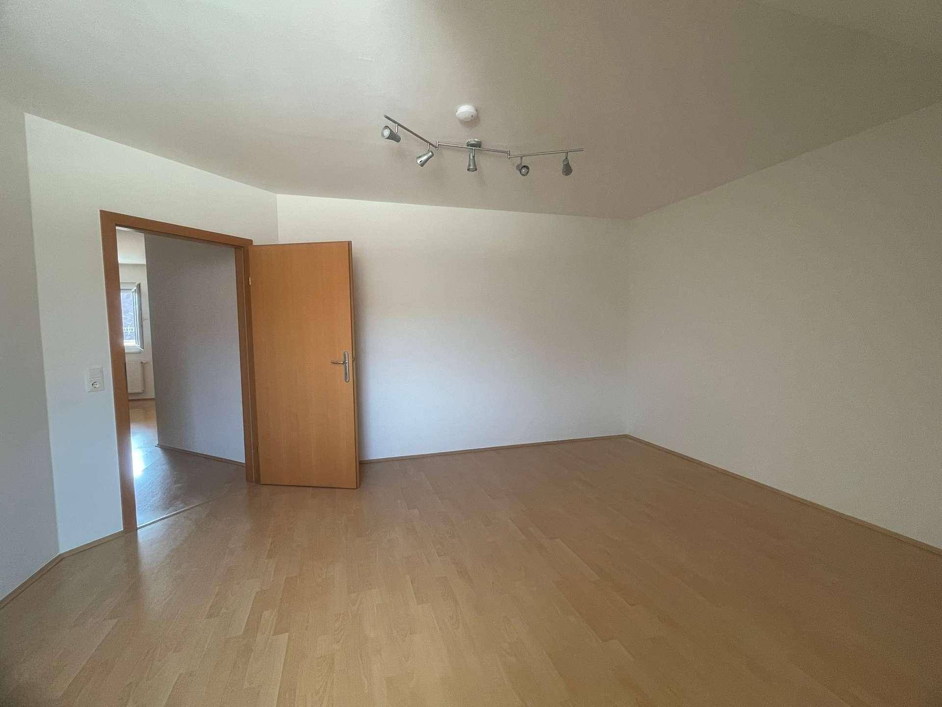 Geräumiges, leeres Zimmer mit hellem Parkettboden und einfacher Deckenbeleuchtung.