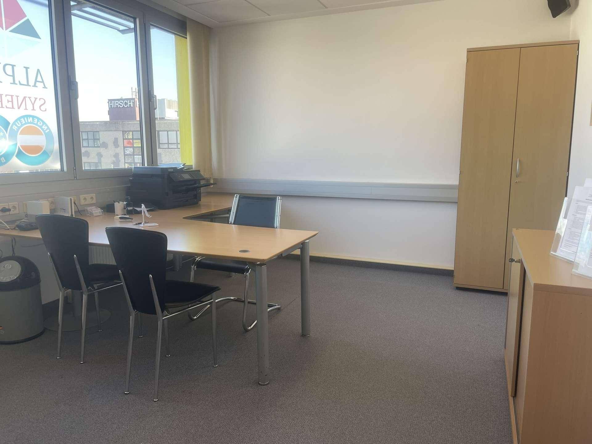 Helles Büro mit Teppichboden, großem Fenster und funktionalen Büromöbeln.