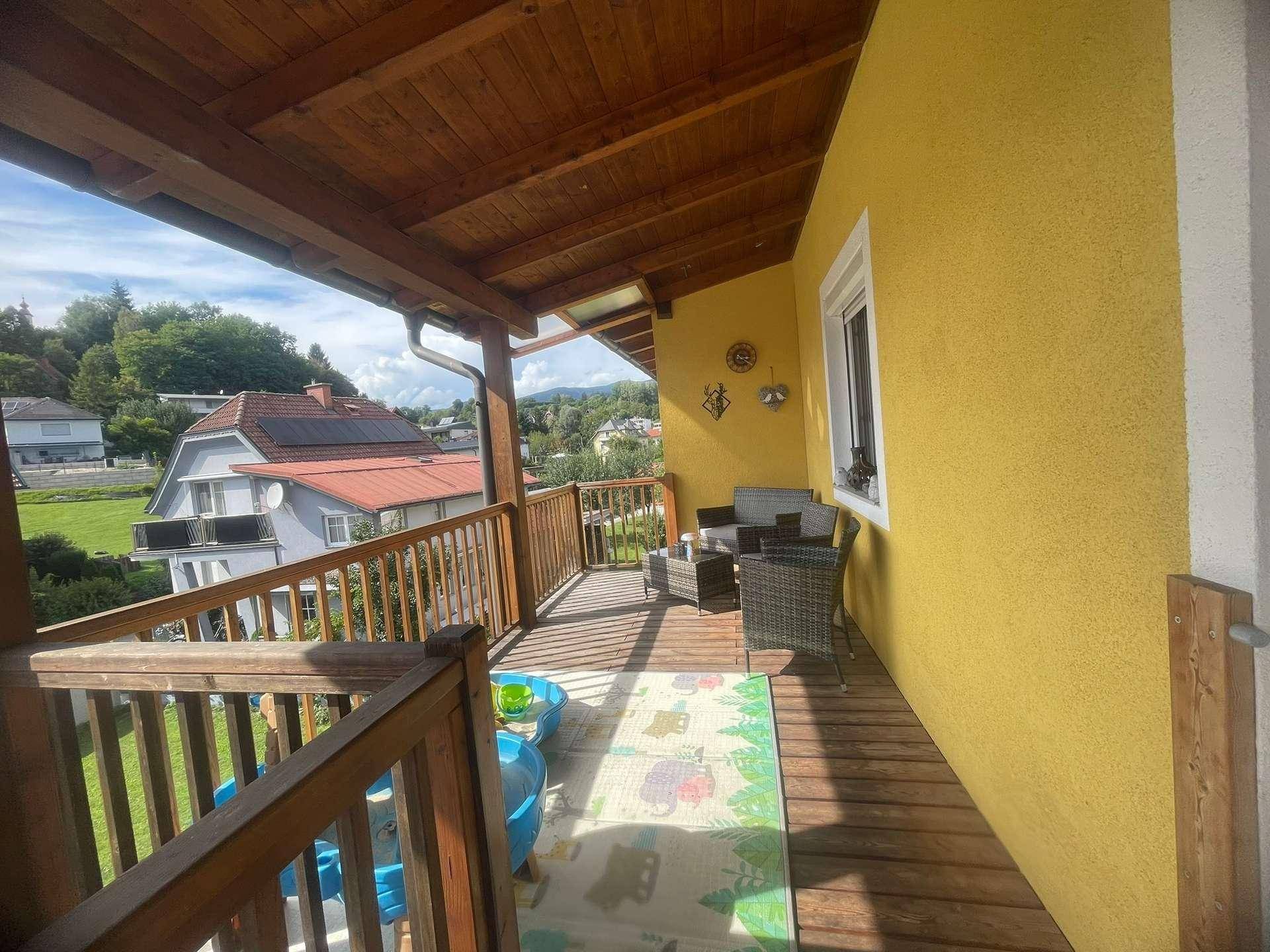 Überdachter Holzbalkon mit Sitzgelegenheiten und Blick auf die grüne Hügellandschaft.