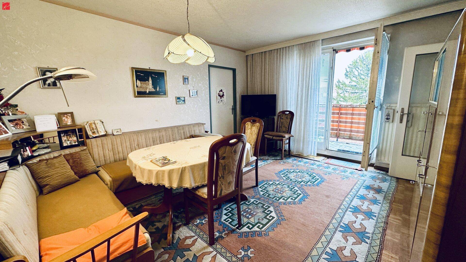 Gemütlicher Wohn- und Essbereich mit Teppichboden und Zugang zum Balkon.
