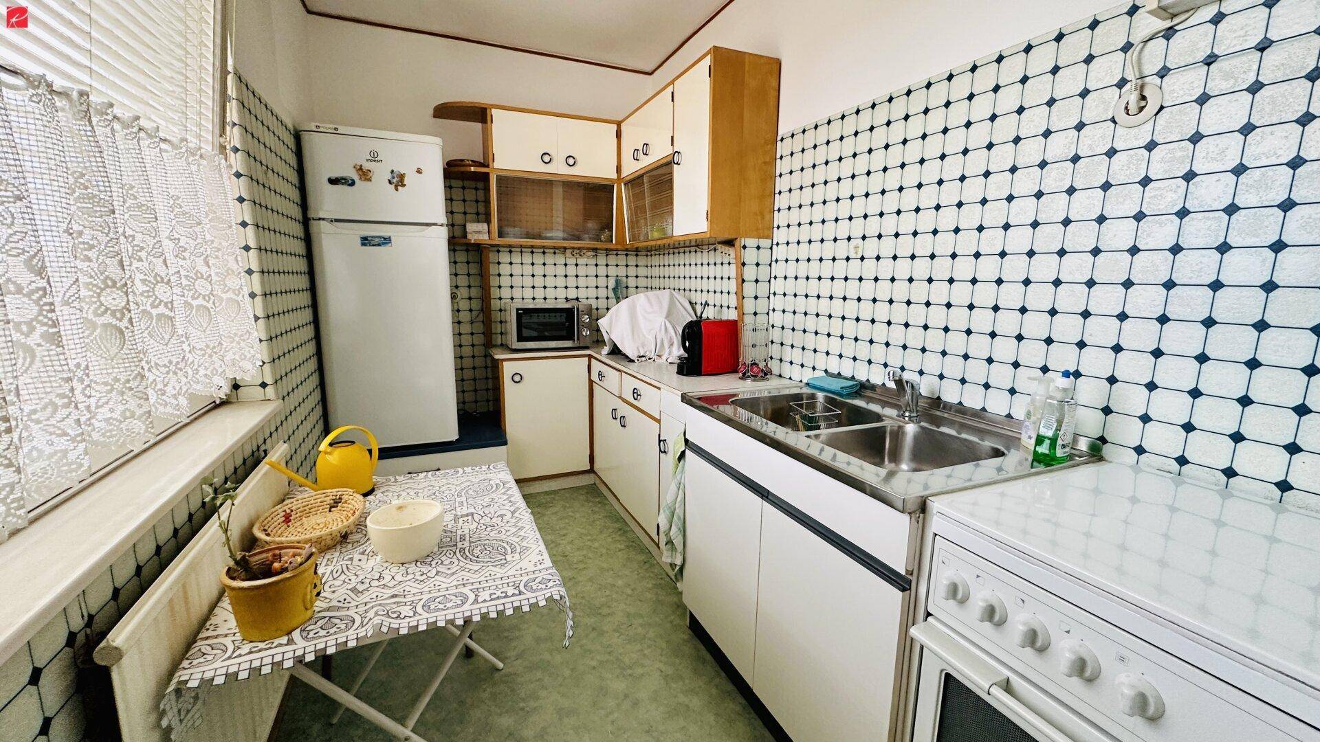 Funktionale Küche mit Fliesenwand, Kühlschrank und Spülbecken.