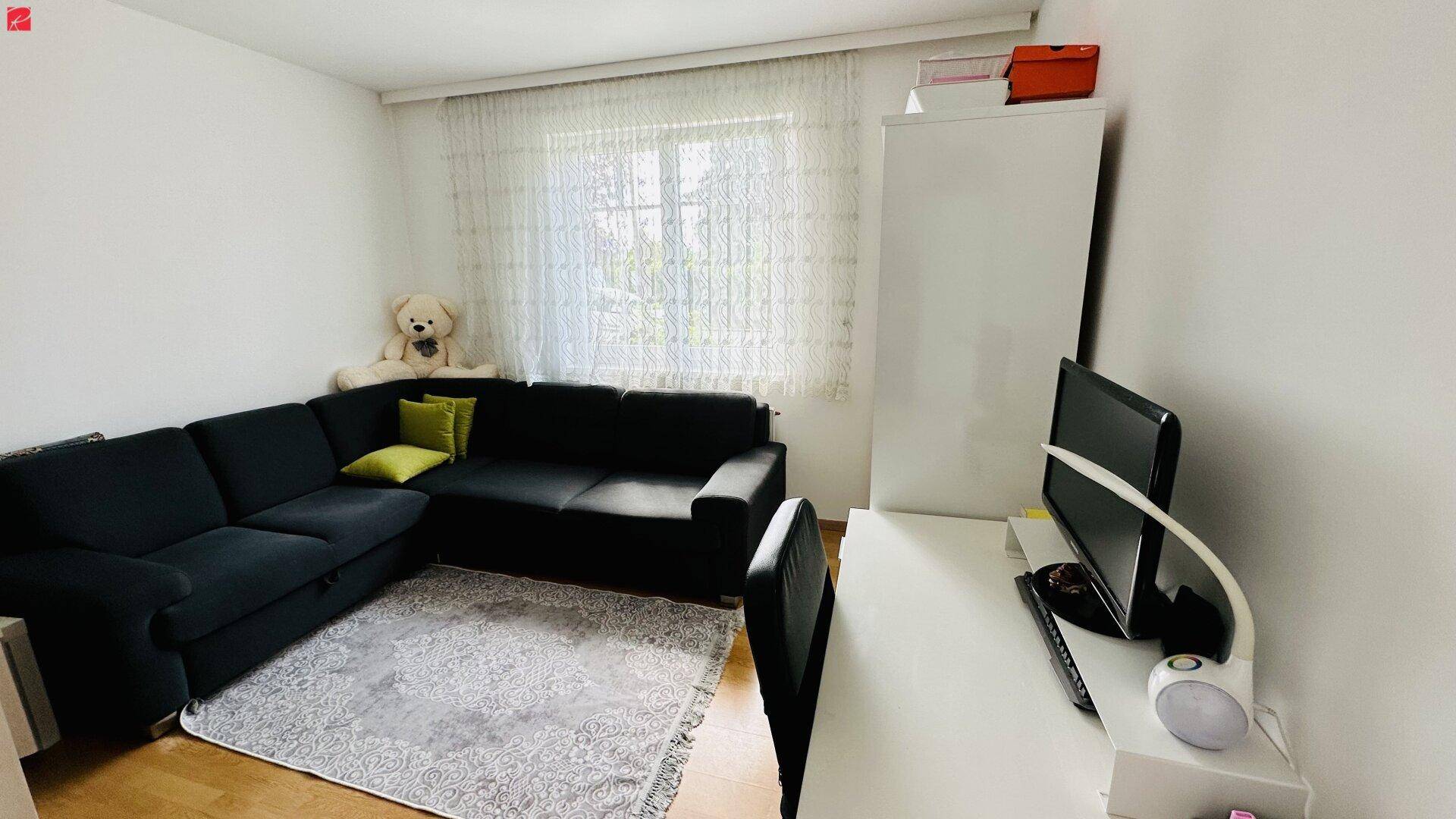 Helles Wohnzimmer mit Ecksofa, Schreibtisch und Fenster, ideal für Entspannung und Arbeit.