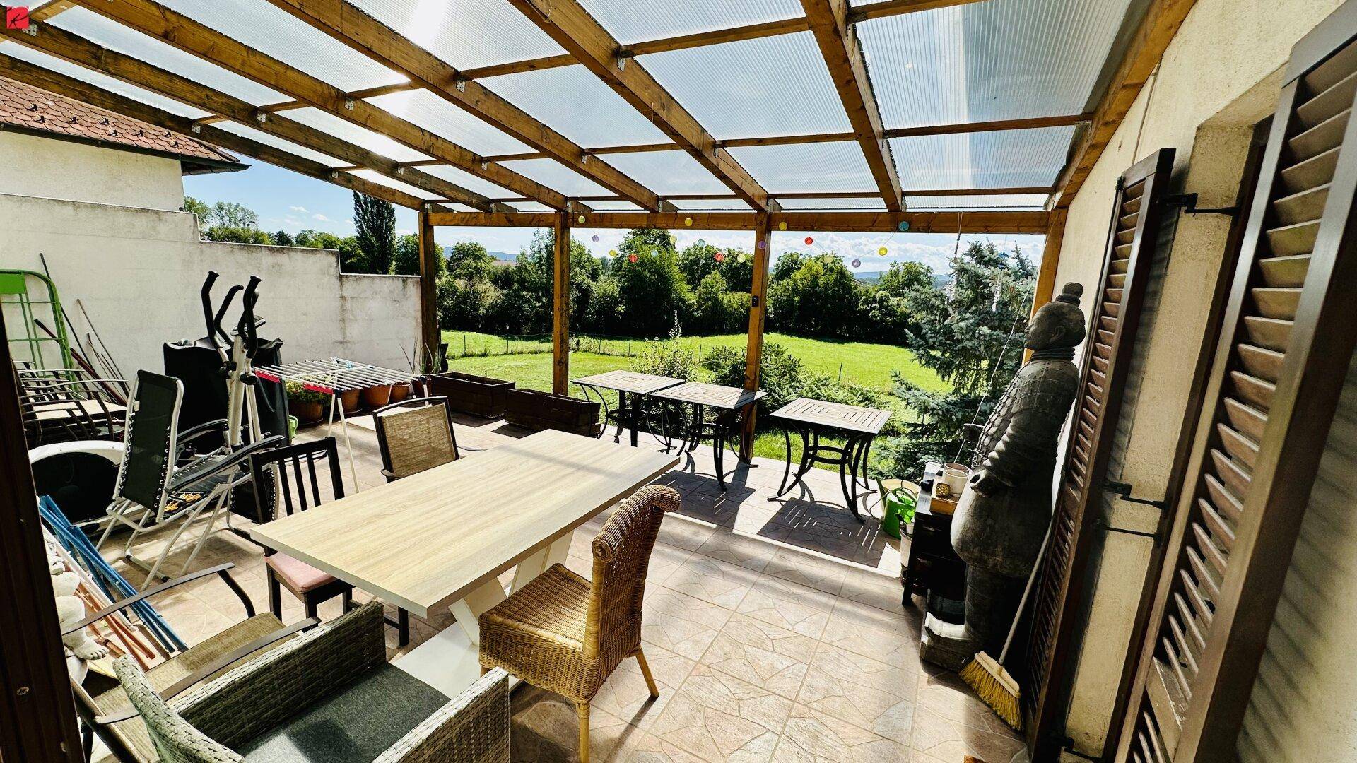 Überdachte Terrasse mit Sitzgelegenheiten und weitem Blick ins Grüne.
