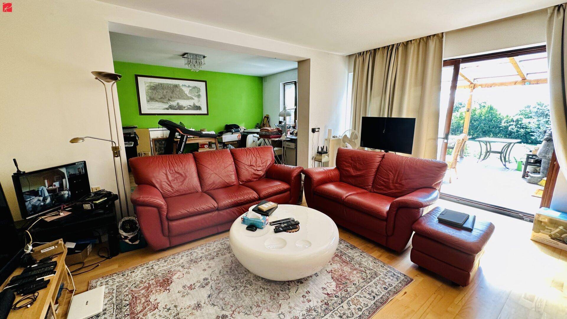 Gemütliches Wohnzimmer mit roten Ledersofas, Teppich und Zugang zur Terrasse.