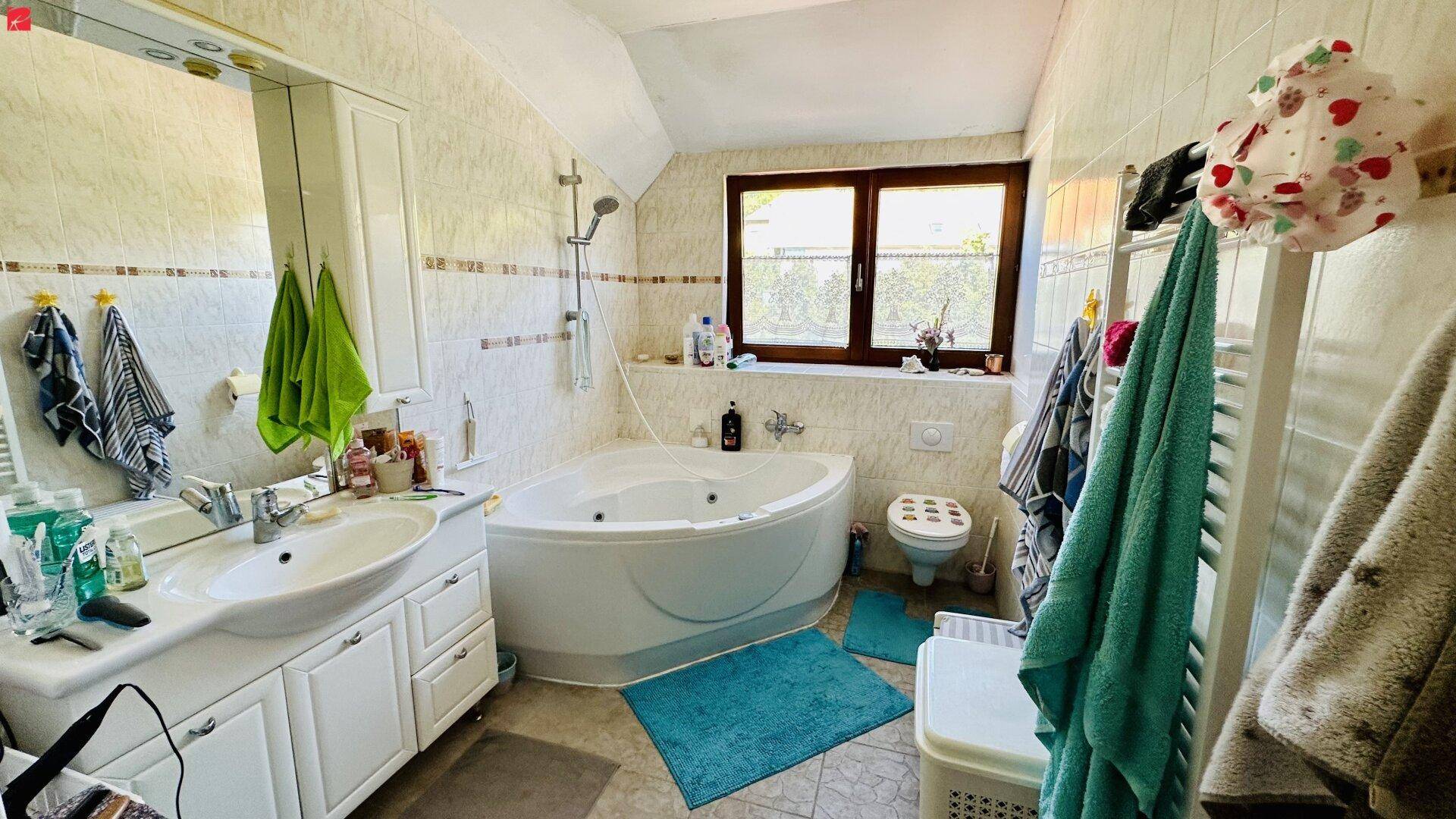 Helles Badezimmer mit Eckbadewanne, Dusche, WC und Fenster.