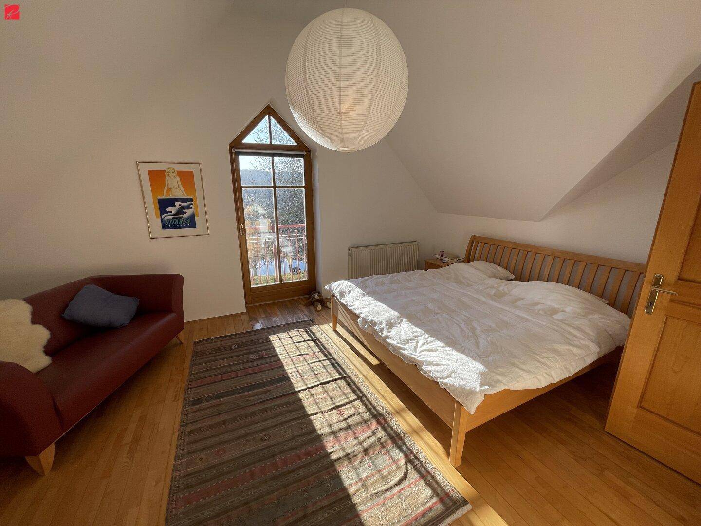 Gemütliches Schlafzimmer mit Holzbett, Dachschräge und Zugang zu einem kleinen Balkon mit Weitblick.