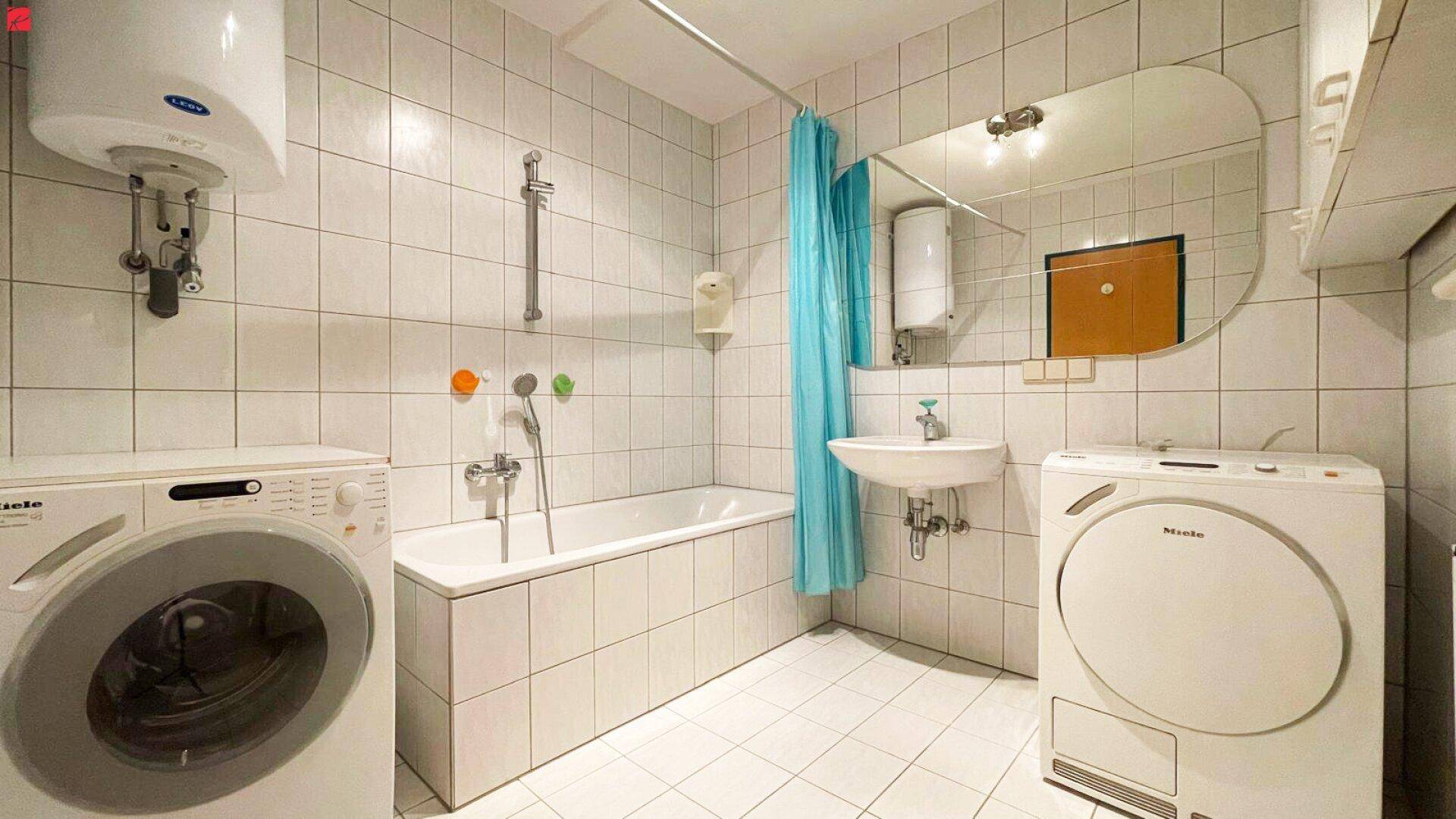 Funktionales Badezimmer mit Badewanne, Waschmaschine und Trockner in weiß gefliestem Raum.