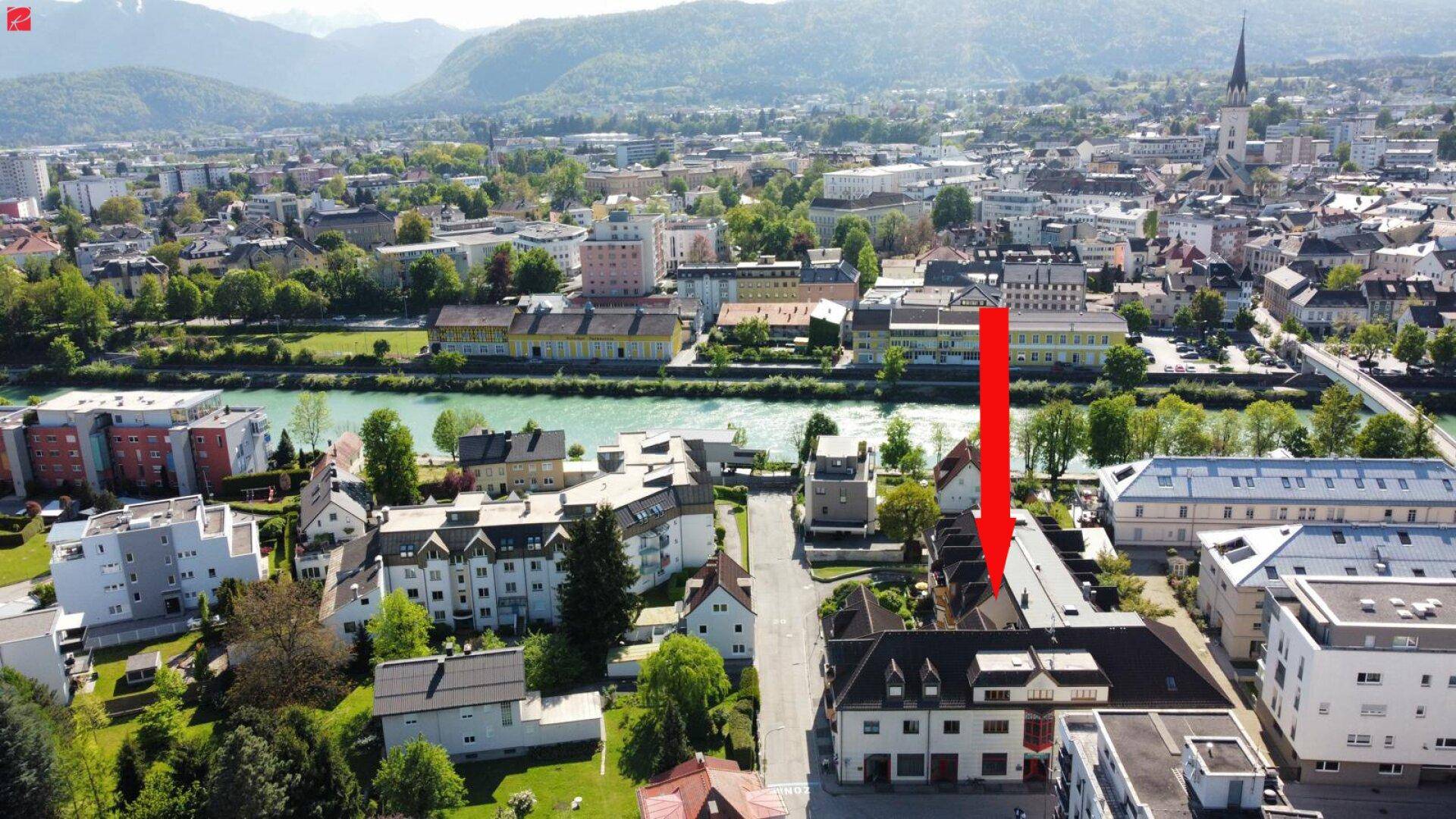 Luftaufnahme einer Stadt mit Fluss, Bergen im Hintergrund und Wohngebäuden.