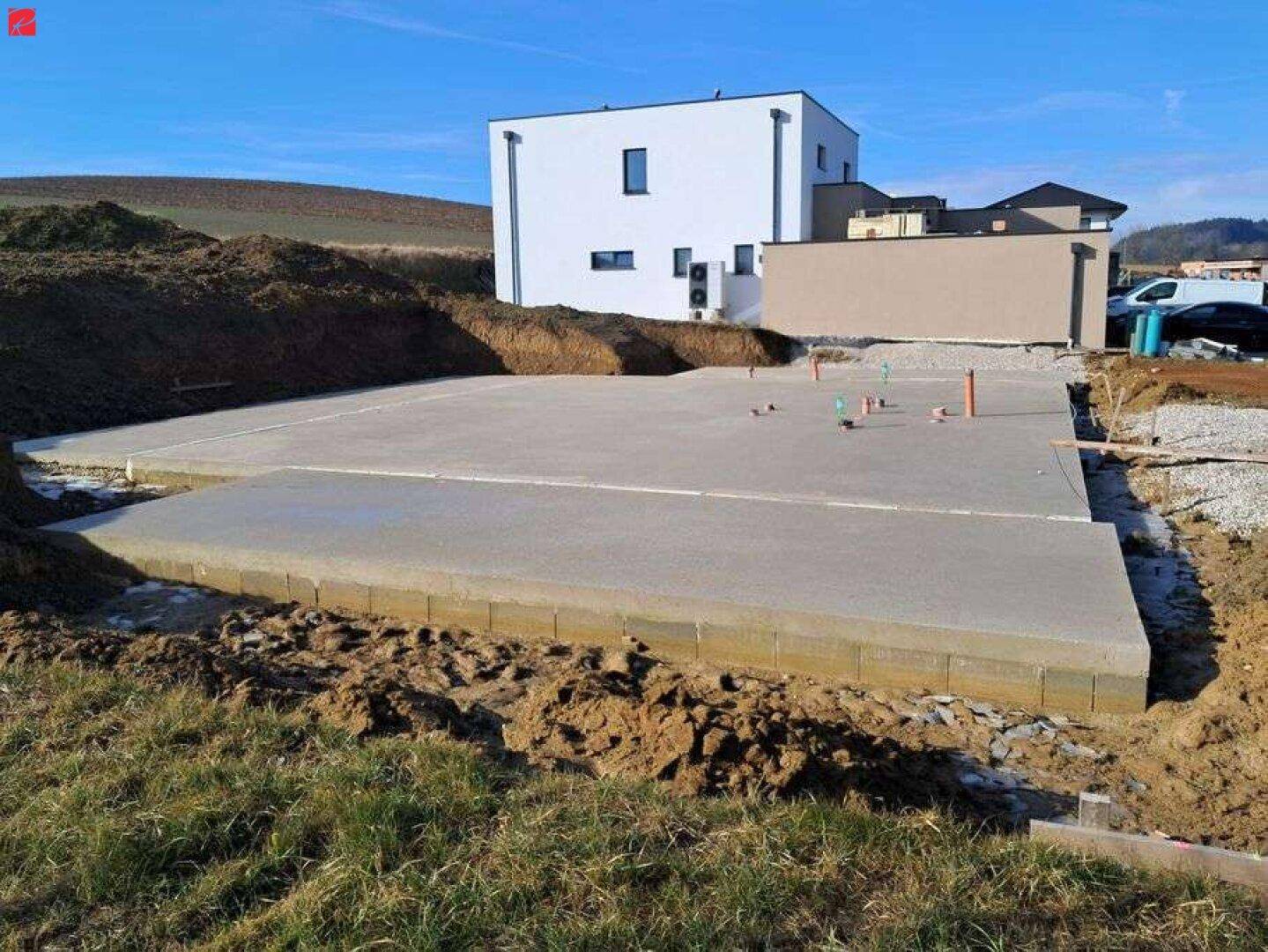 Neubau-Fundament mit bereits errichtetem Nachbargebäude im Hintergrund.