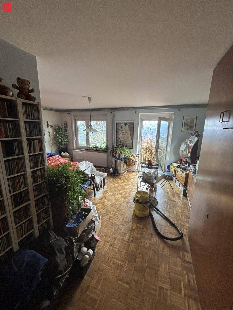Helles Wohnzimmer mit Parkettboden, Bücherregal und Zugang zu einem Außenbereich mit Weitblick.