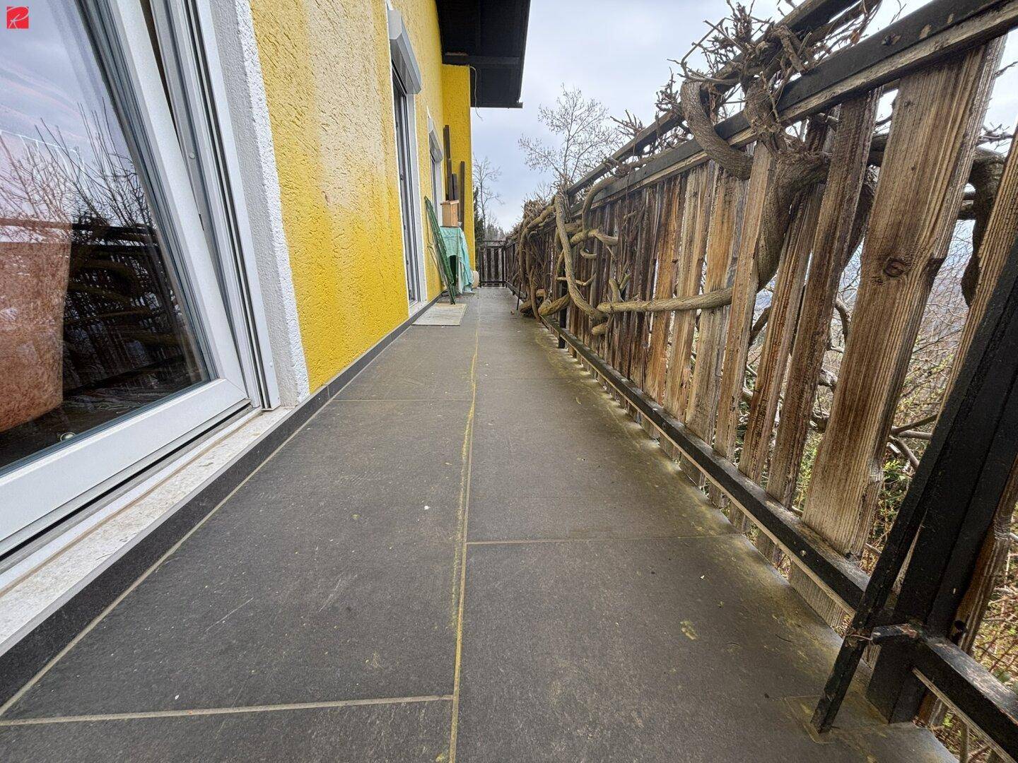 Langer Balkon mit Fliesenboden und rustikalem Holzgeländer, ideal für entspannte Stunden im Freien.
