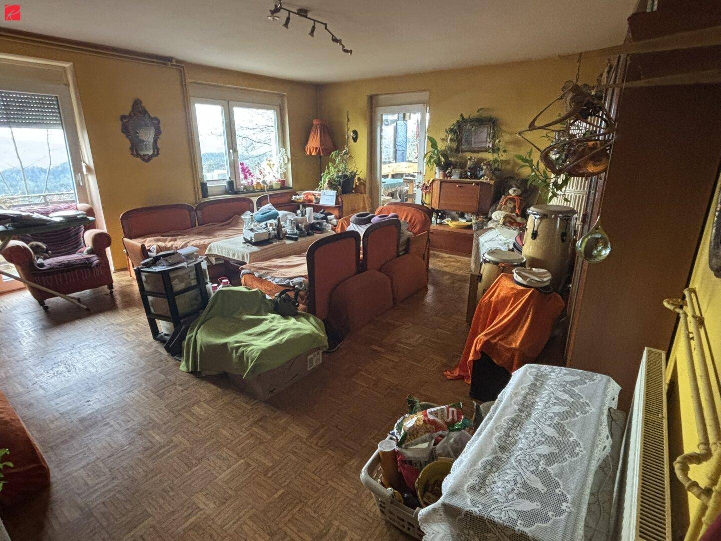 Geräumiges Wohnzimmer mit Parkettboden, großen Fenstern und gemütlichen Sitzgelegenheiten mit Ausblick.
