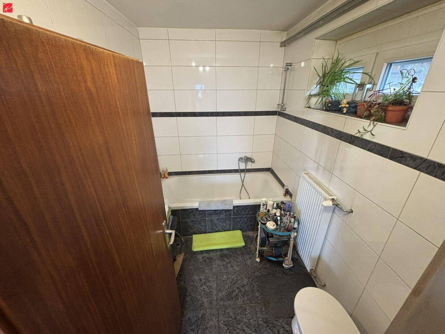 Gefliestes Badezimmer mit Badewanne, Fenster und dunklem Boden in Standardausstattung.