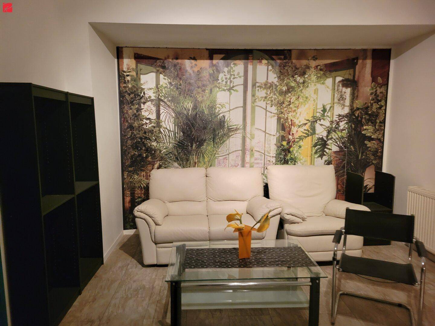 Gemütliches Wohnzimmer mit beigefarbenen Sofas, einem Glastisch und einer Wandtapete mit Pflanzenmotiv.