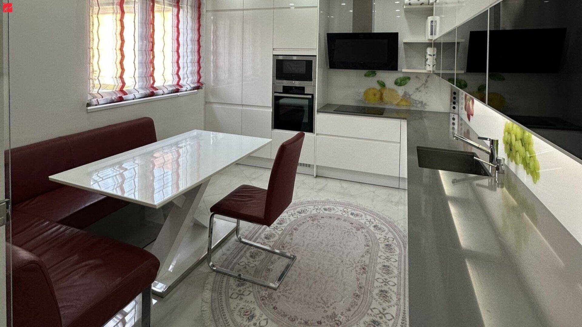 Moderne Küche mit weißen Hochglanzfronten, dunkler Arbeitsplatte und integriertem Essbereich mit roter Sitzbank.