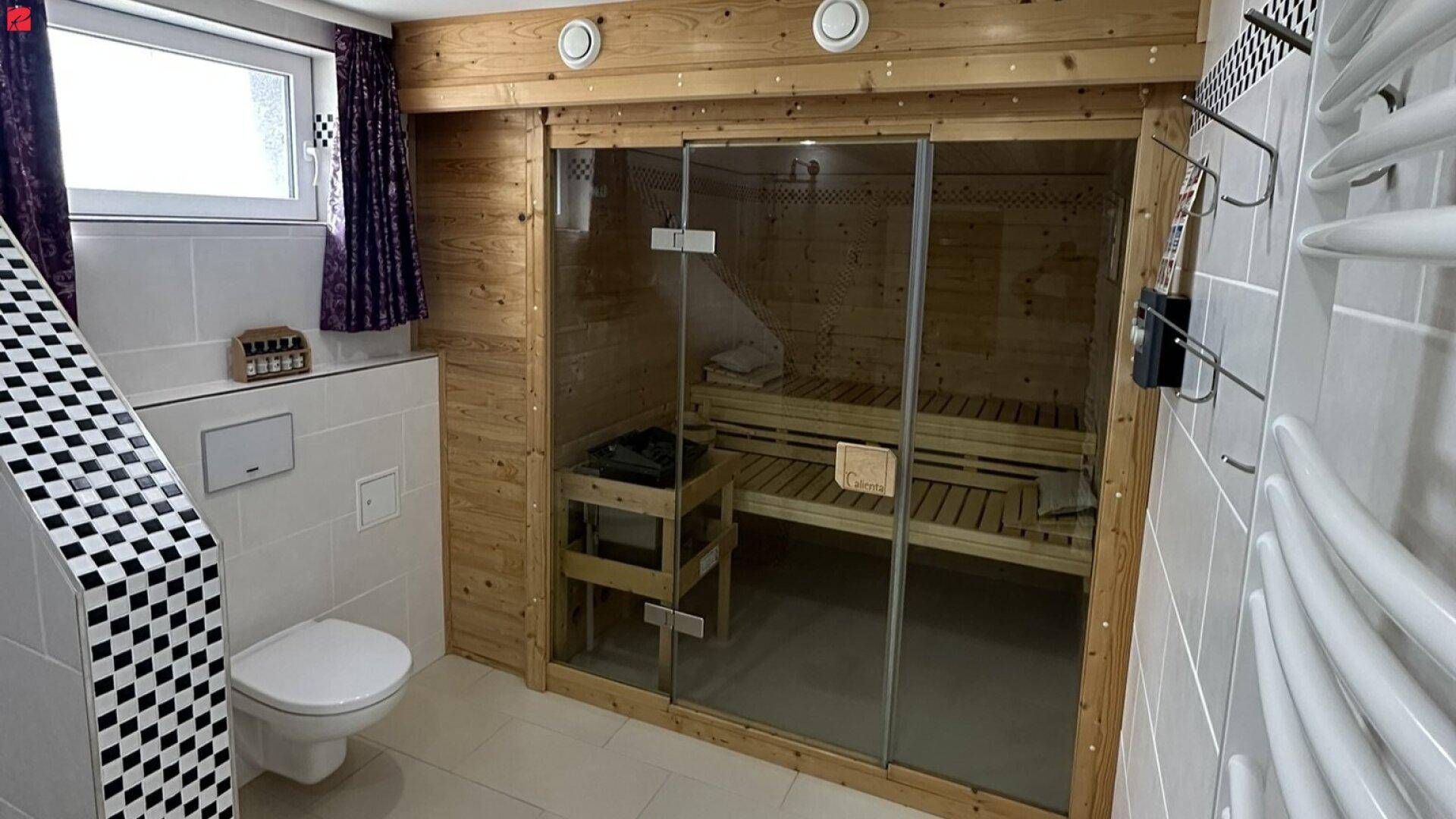 Modernes Badezimmer mit integrierter Sauna, WC und beheiztem Handtuchhalter, teilweise gefliest.