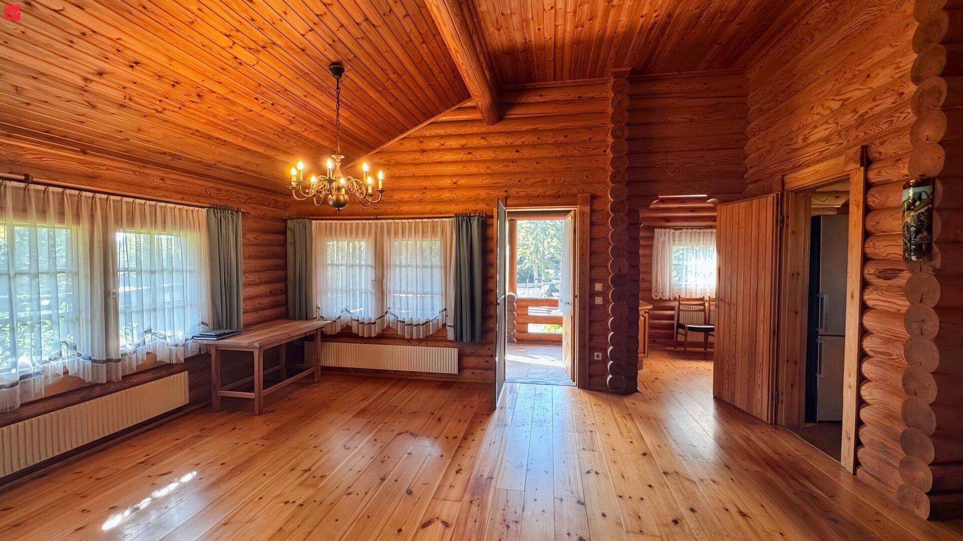 Geräumiges Wohnzimmer im Blockhausstil mit Holzboden, Holzdecken und Zugang zu einem Balkon.