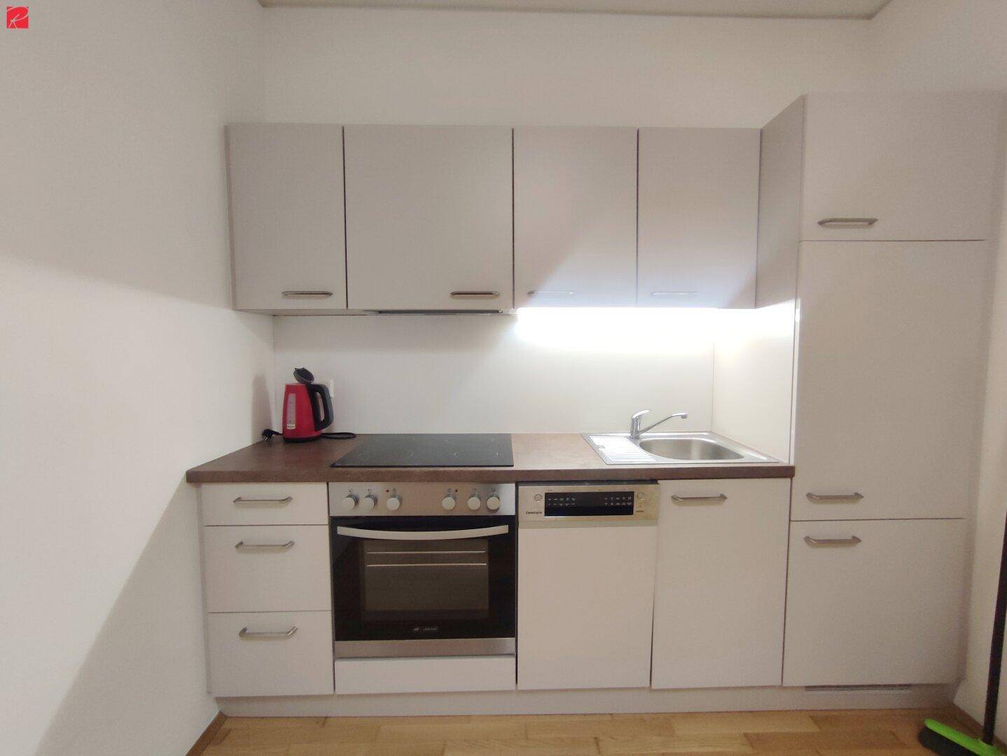 Moderne Küchenzeile mit hellen Schränken, integrierten Geräten und Holzboden.