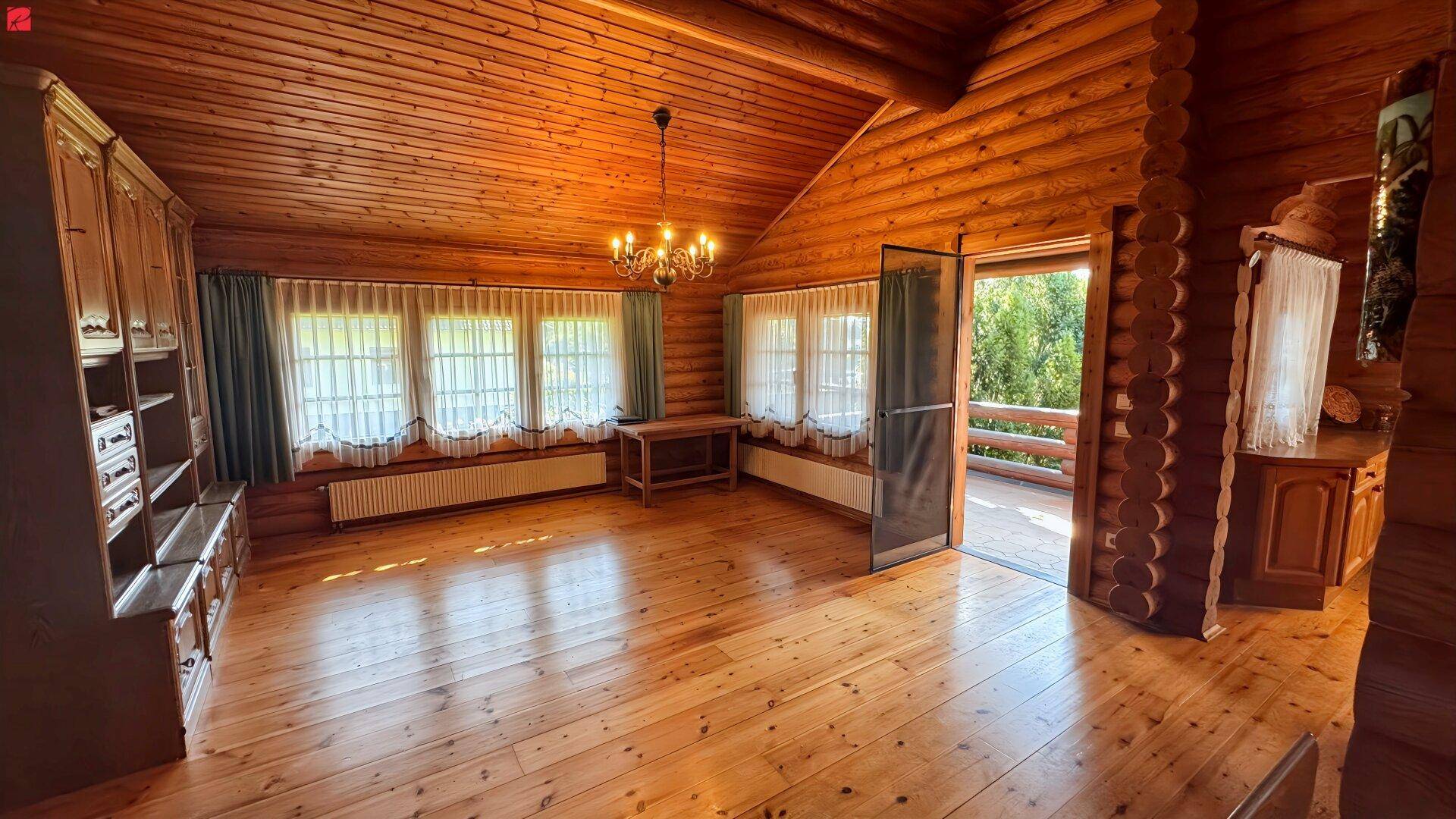 Helles Wohnzimmer mit viel Holz, einem Kronleuchter und Zugang zu einem sonnigen Außenbereich.